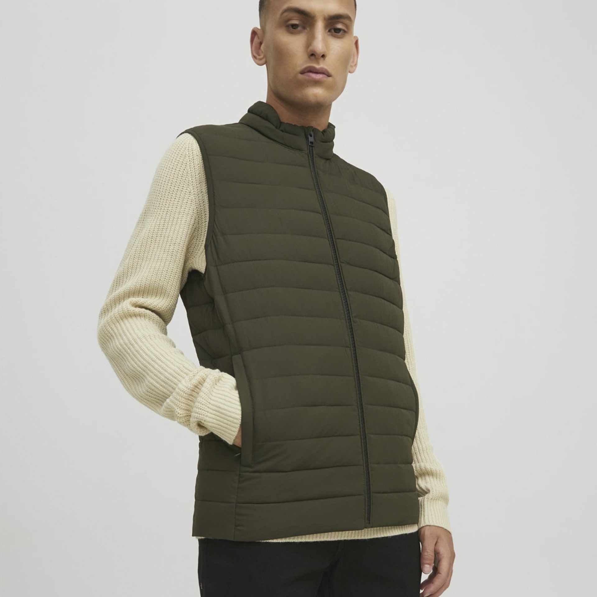 Colete acolchoado verde-oliva com fecho de correr, usado sobre camisola creme