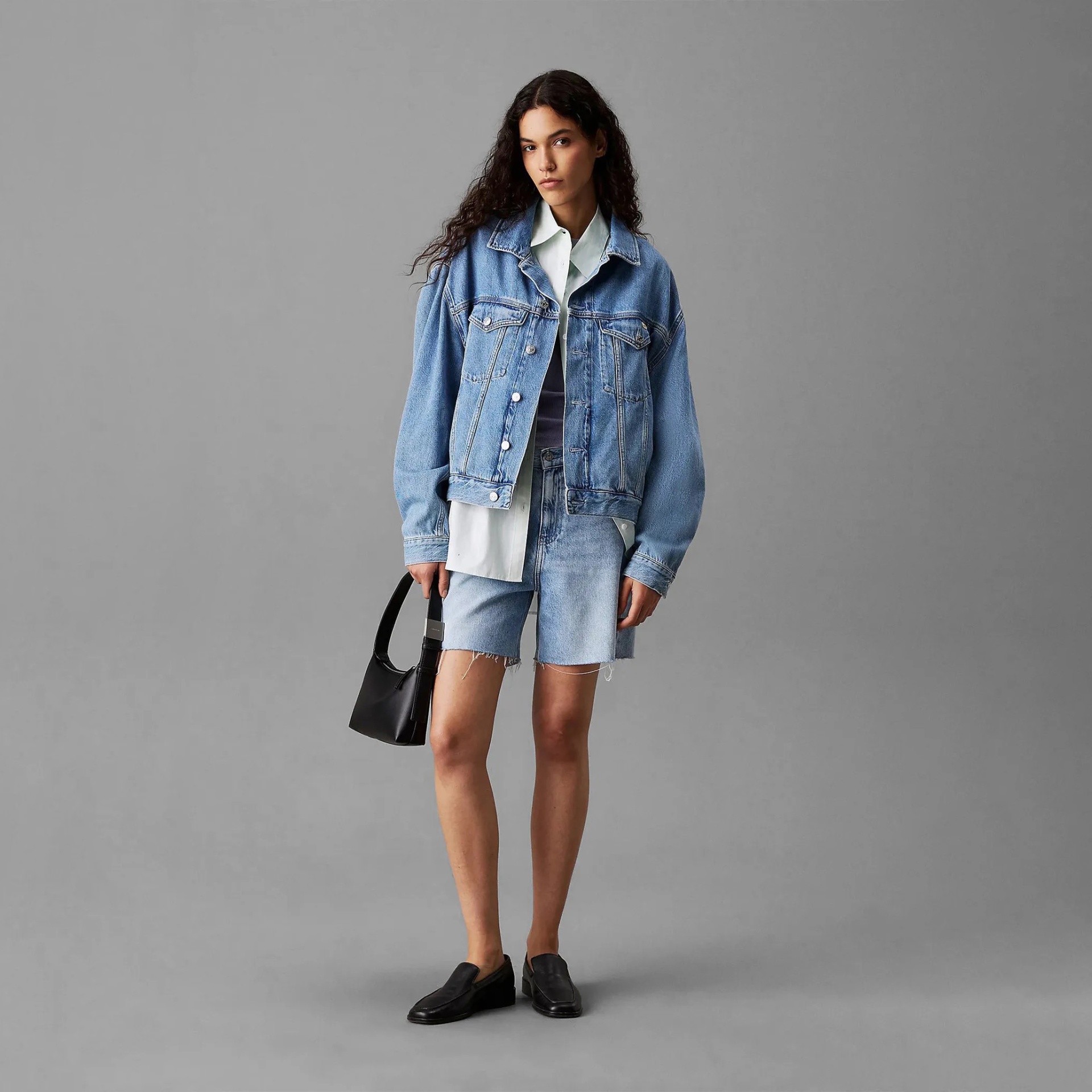 Mulher com casaco de ganga azul claro, calções de ganga, sapatos pretos e mala preta