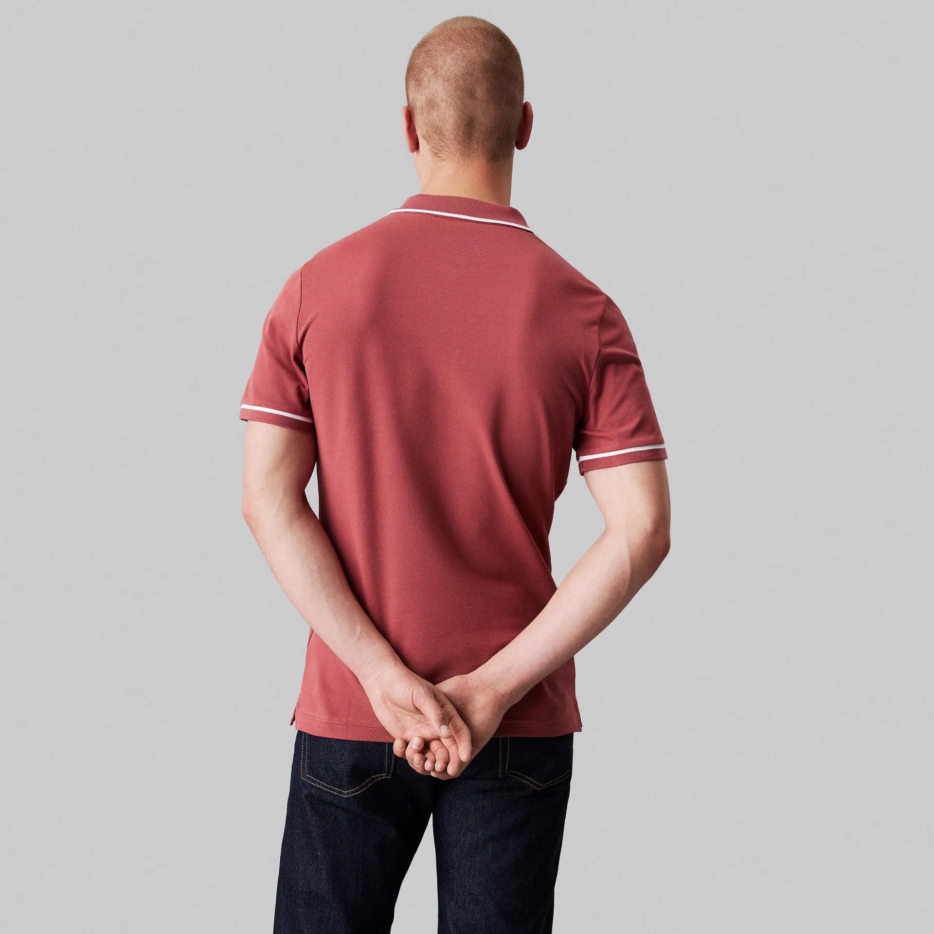 Polo masculino terracota com frisos brancos, visto de costas, com jeans escuros