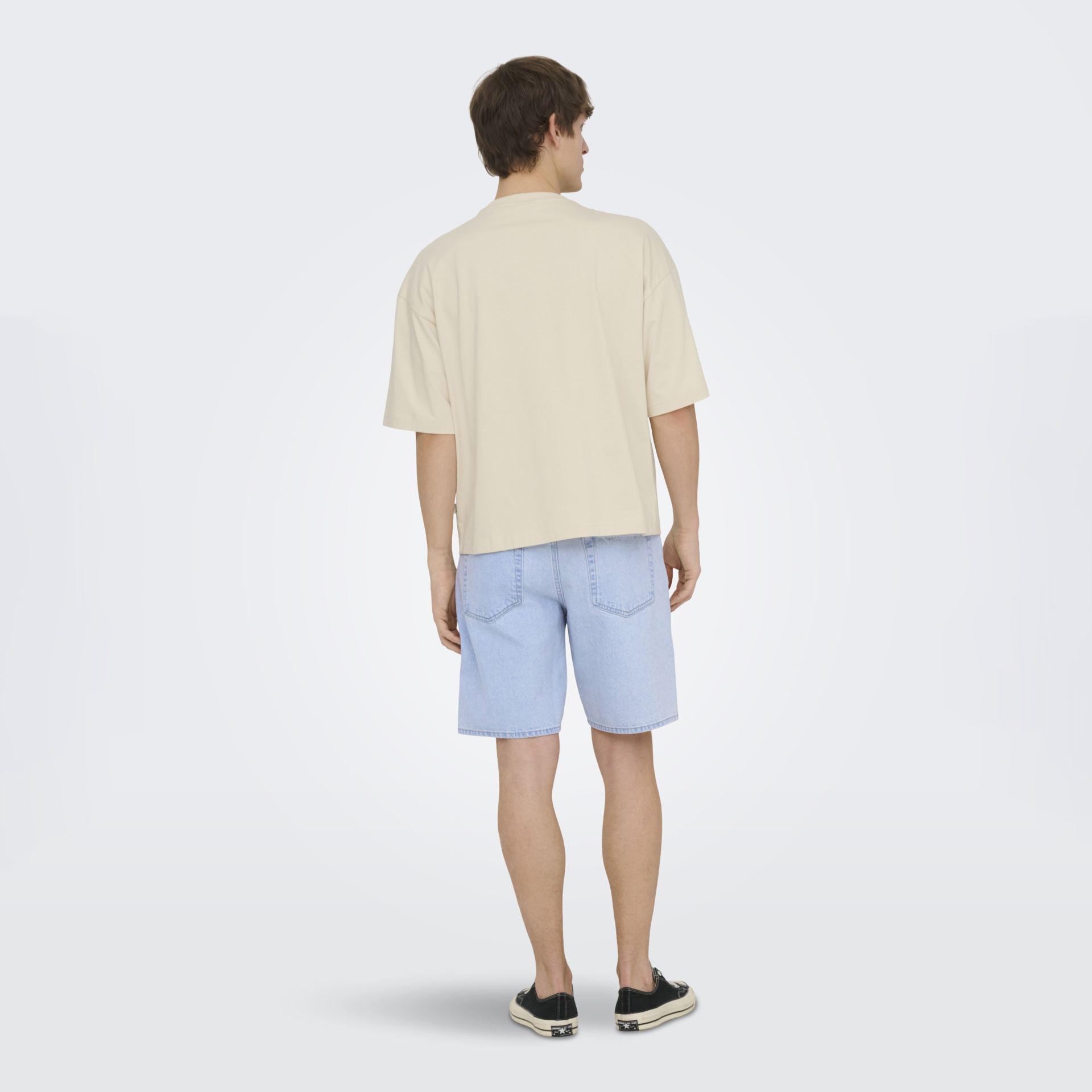 Homem de costas com t-shirt creme e calções de ganga