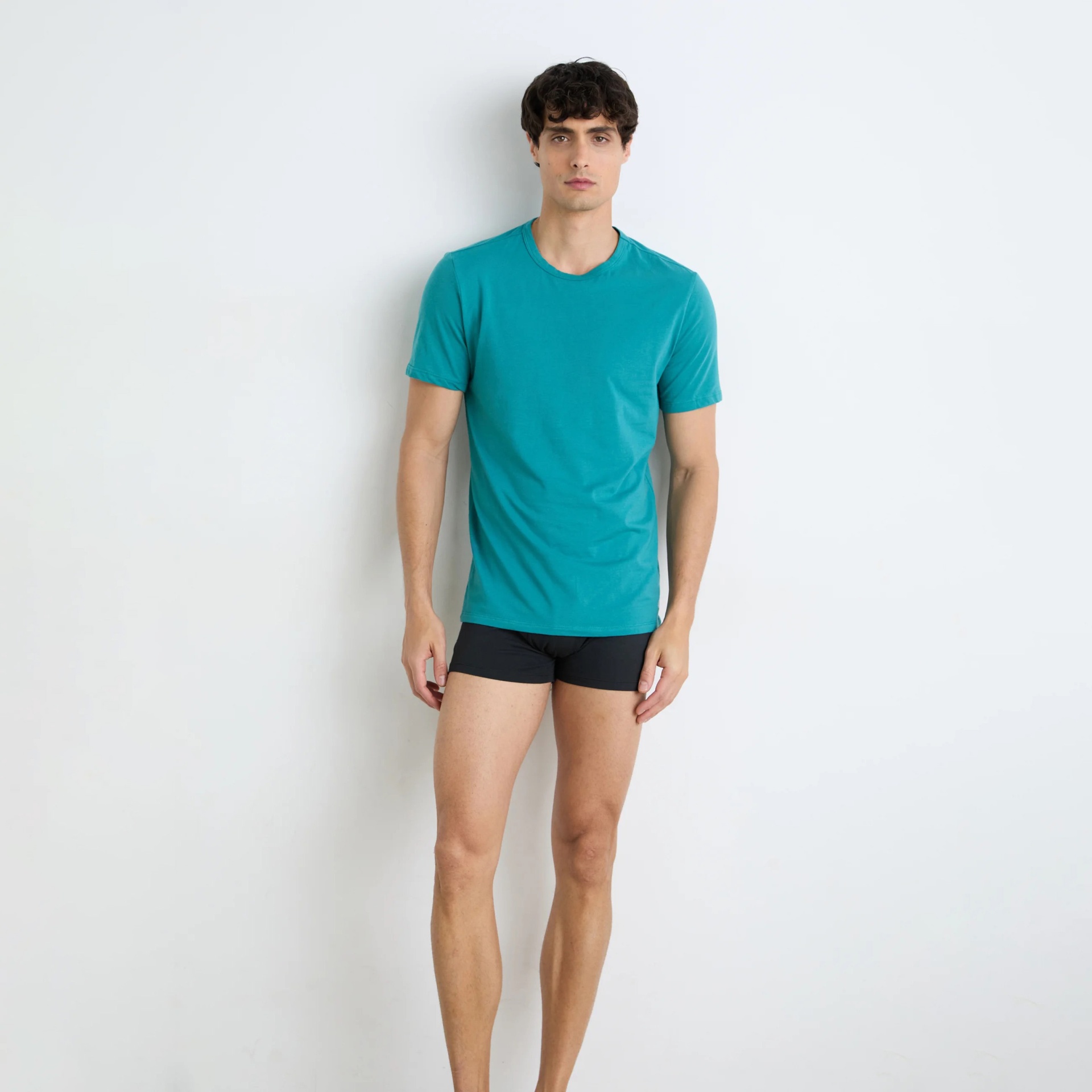 Modelo masculino com t-shirt azul-turquesa e cuecas pretas em fundo branco