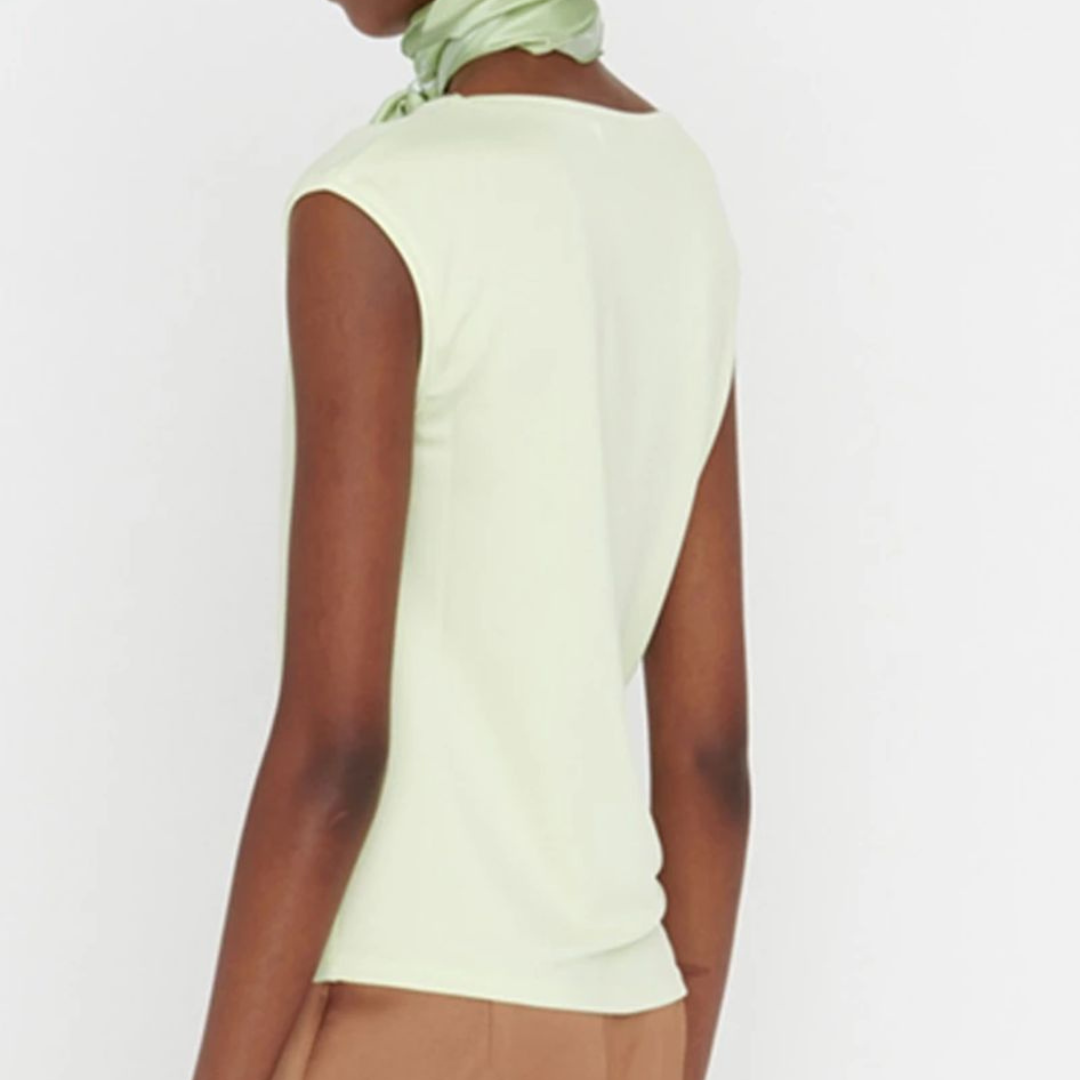 Mulher de costas com camisola sem mangas verde claro e calças castanhas