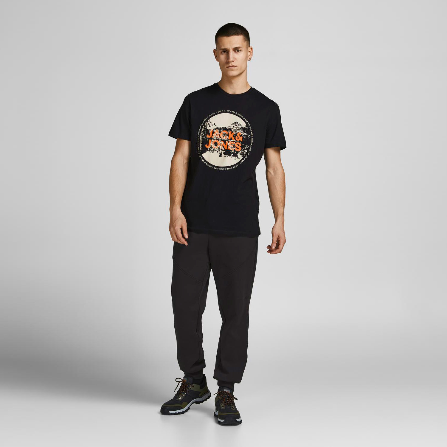 Homem com t-shirt preta Jack & Jones e calças pretas em fundo cinza claro