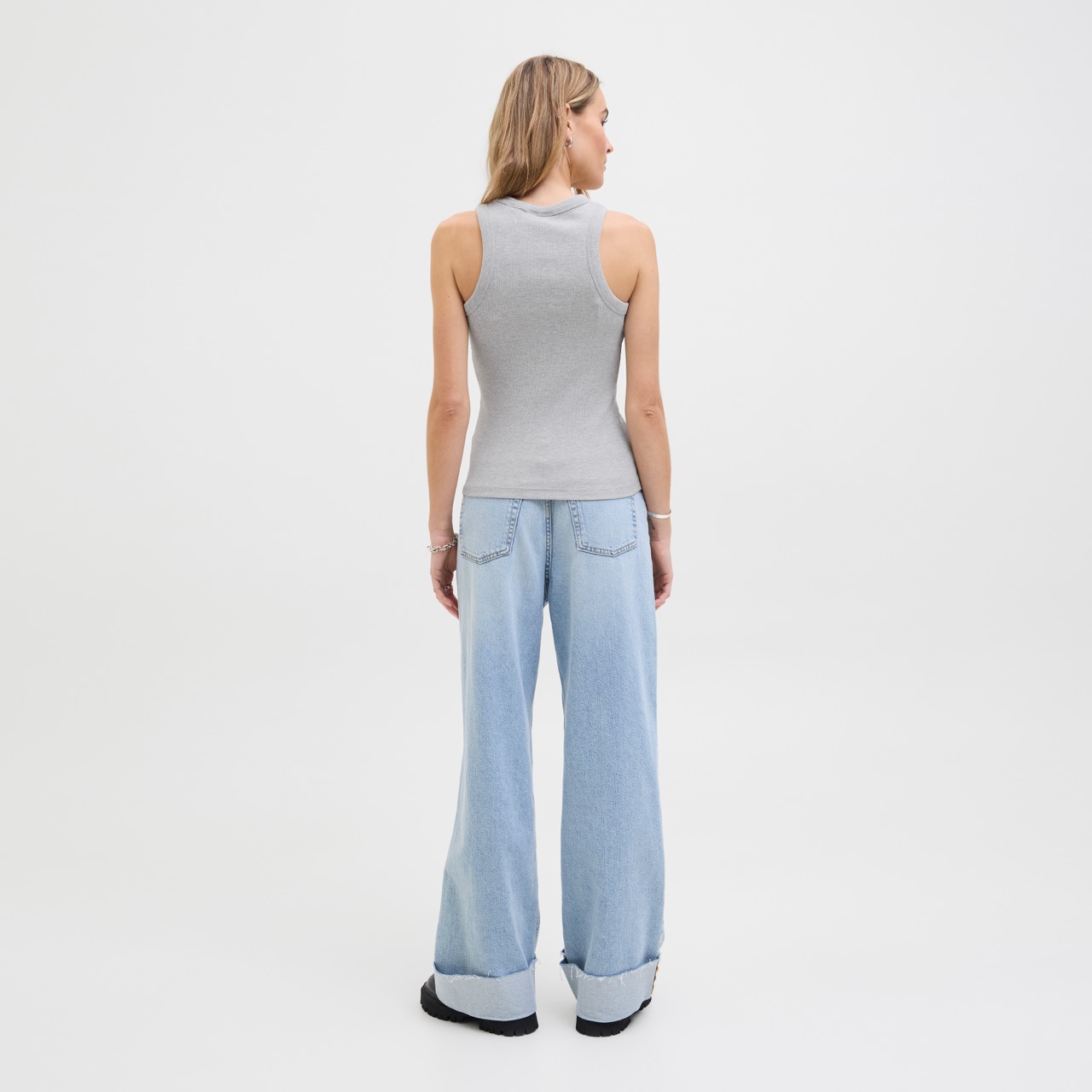 Modelo de costas usando camisola cinzenta de alças e calças largas de ganga azul clara