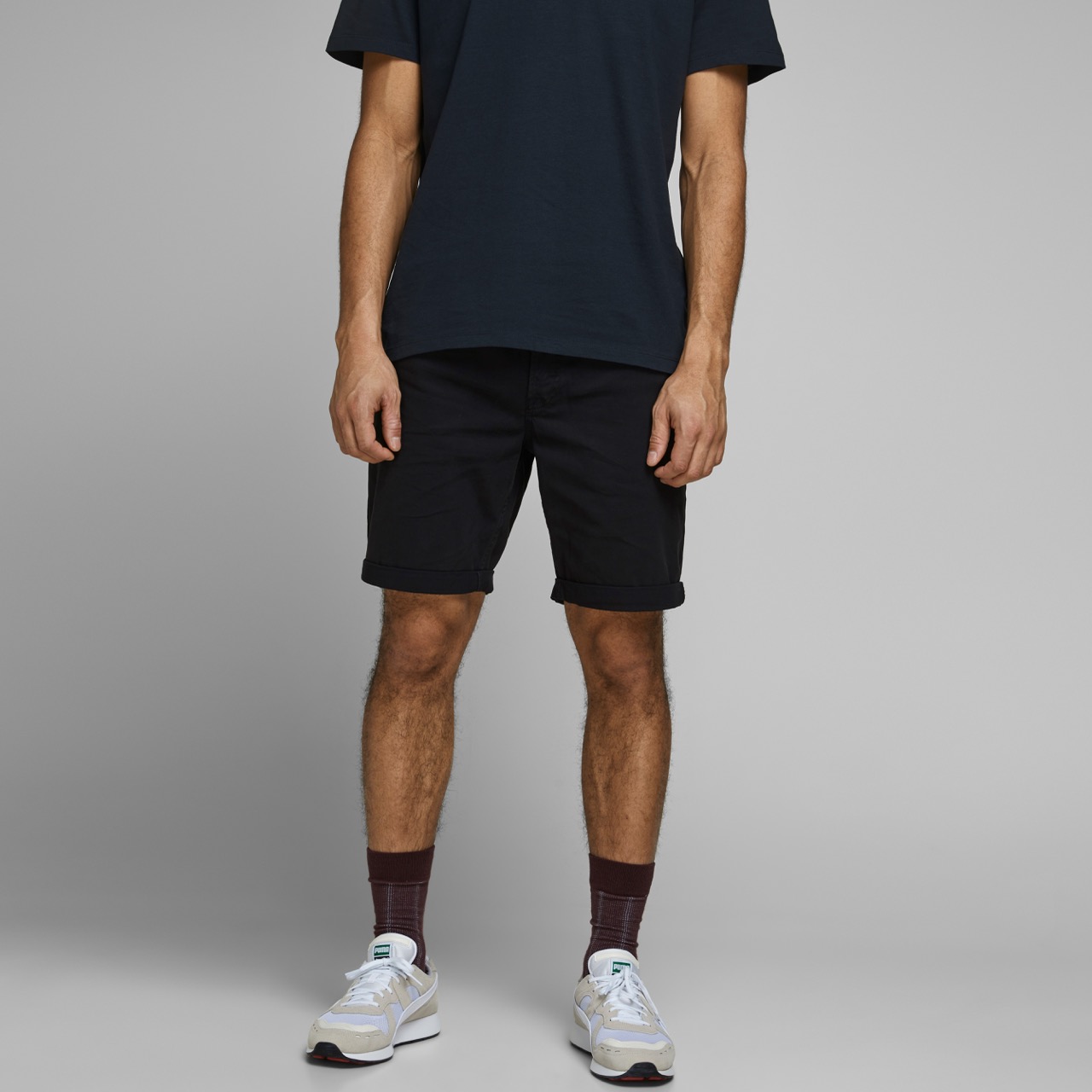 Homem com t-shirt e calções pretos, meias castanhas e sapatilhas brancas