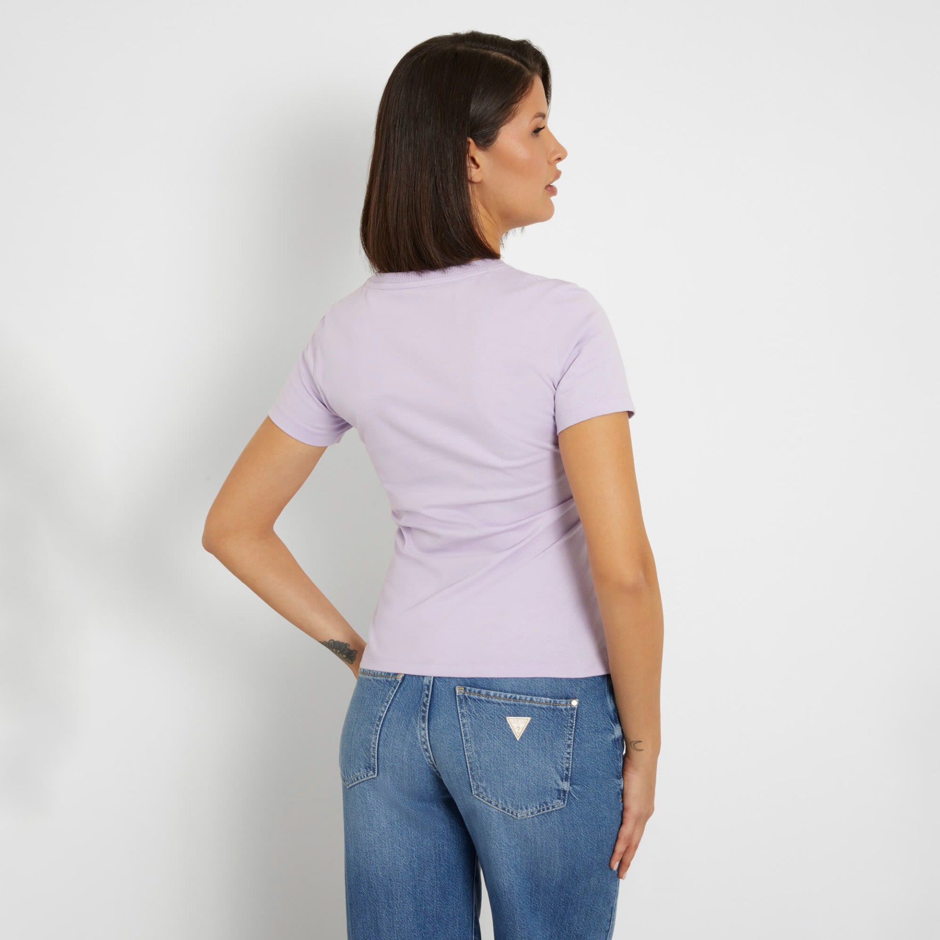 Mulher vista de costas com t-shirt lilás e jeans azuis Guess