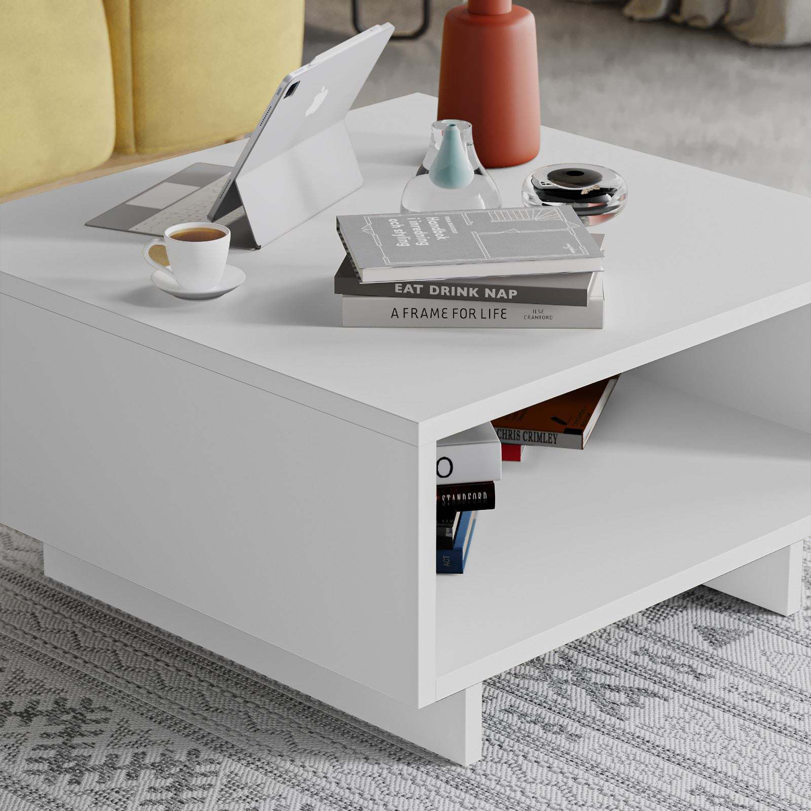 Mesa de centro branca com livros, tablet, café e objetos decorativos em sala de estar.