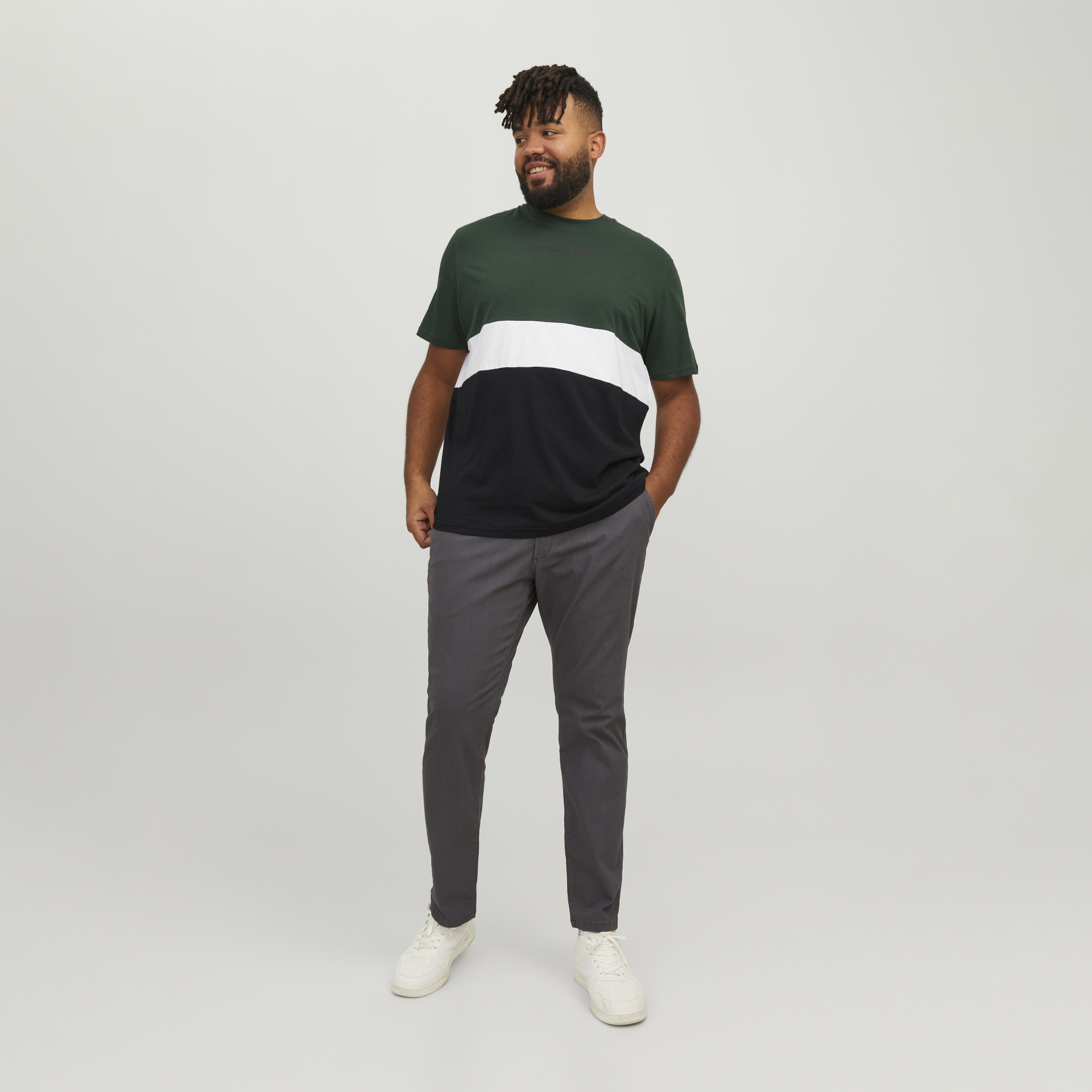 Homem com t-shirt tricolor e calças cinza em fundo cinza claro