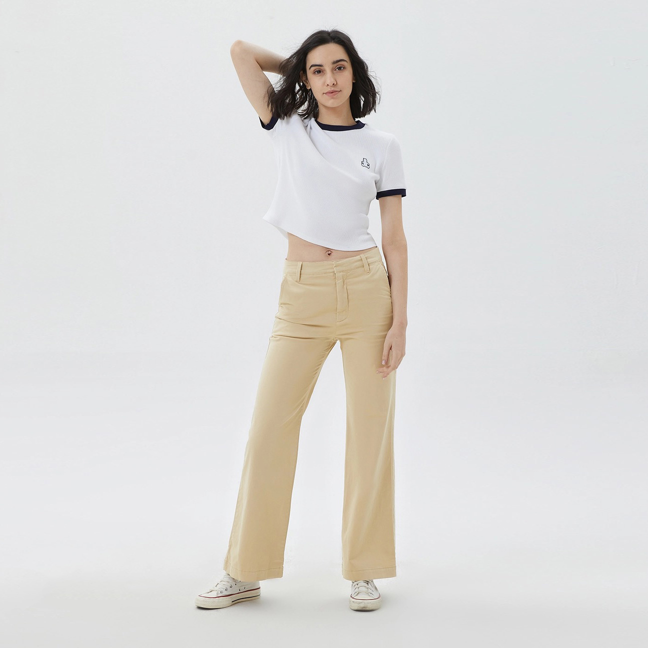 Mulher com t-shirt branca e calças bege em fundo branco