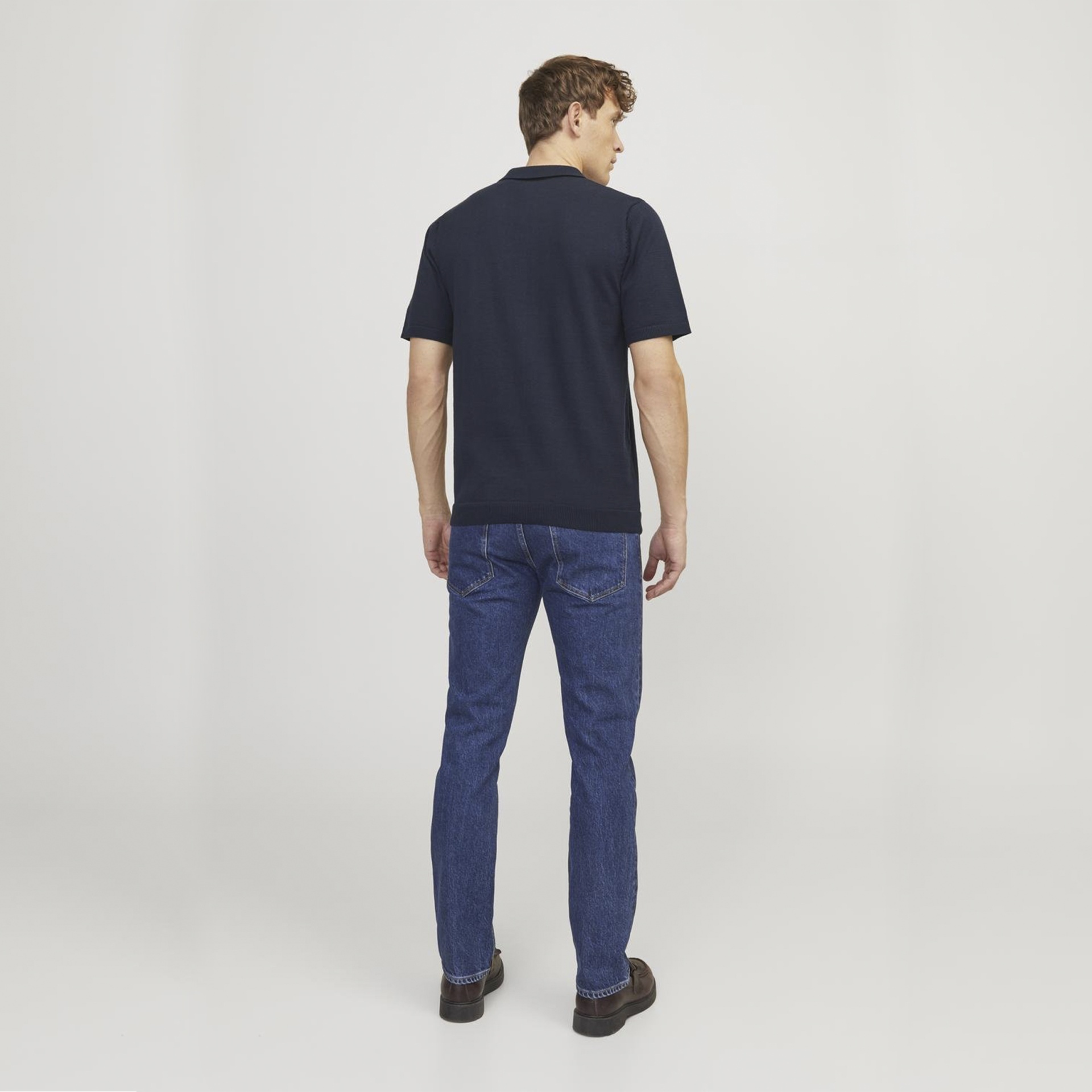 Homem de costas com camisa polo preta e calças de ganga azul escuro