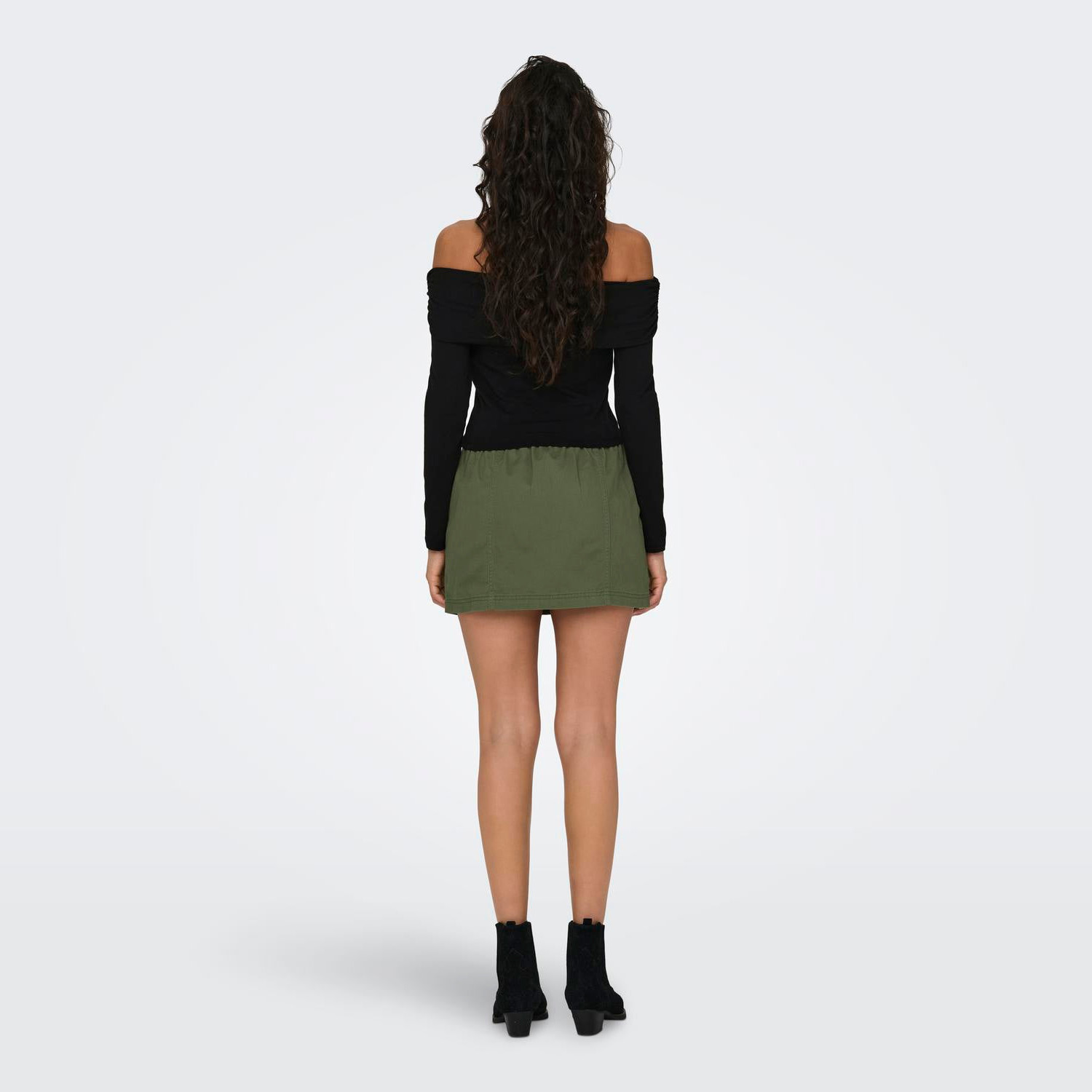 Mulher com blusa preta, saia verde e botas pretas vista de costas