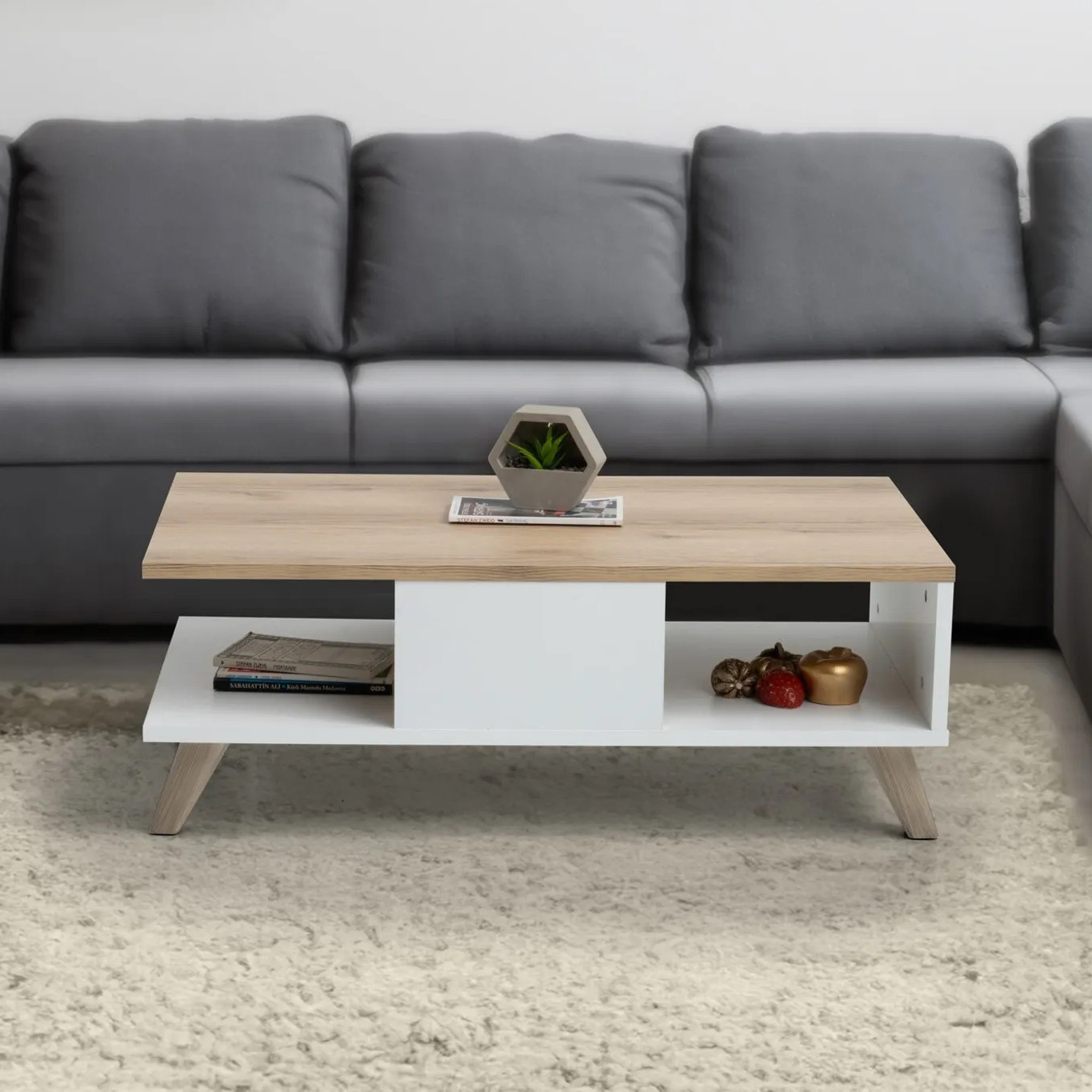 Mesa de centro em madeira clara e branca com decoração e sofá cinza ao fundo