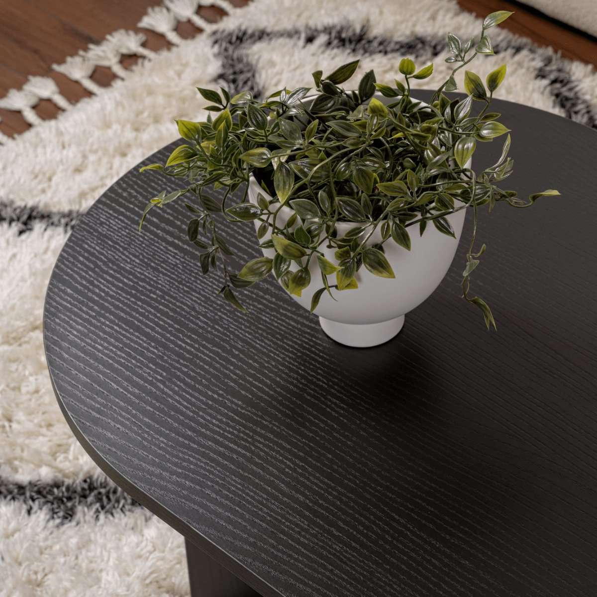 Mesa de centro preta redonda com vaso branco e planta artificial em tapete branco e cinza