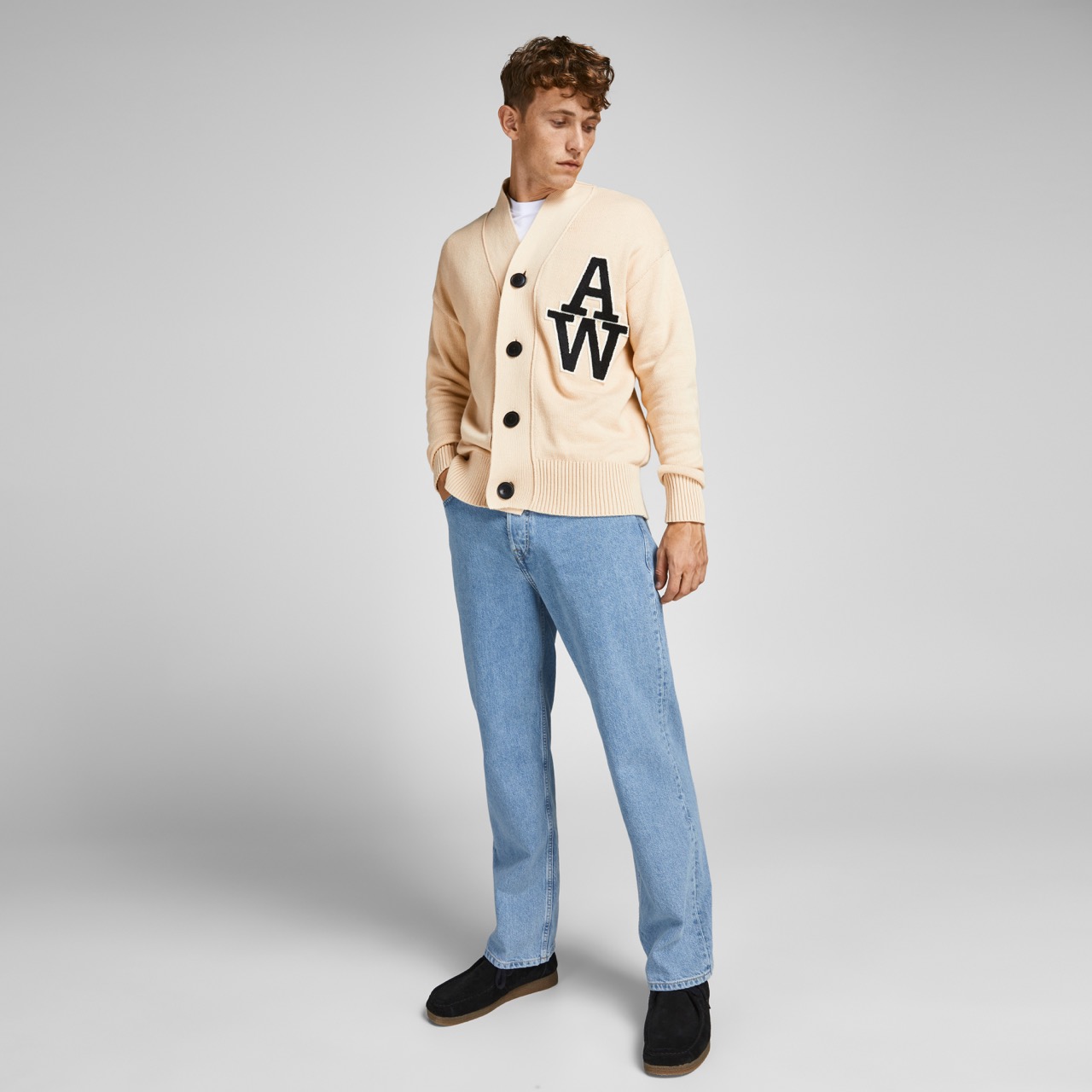 Homem a usar camisola creme com letras AW, jeans azuis e sapatos pretos