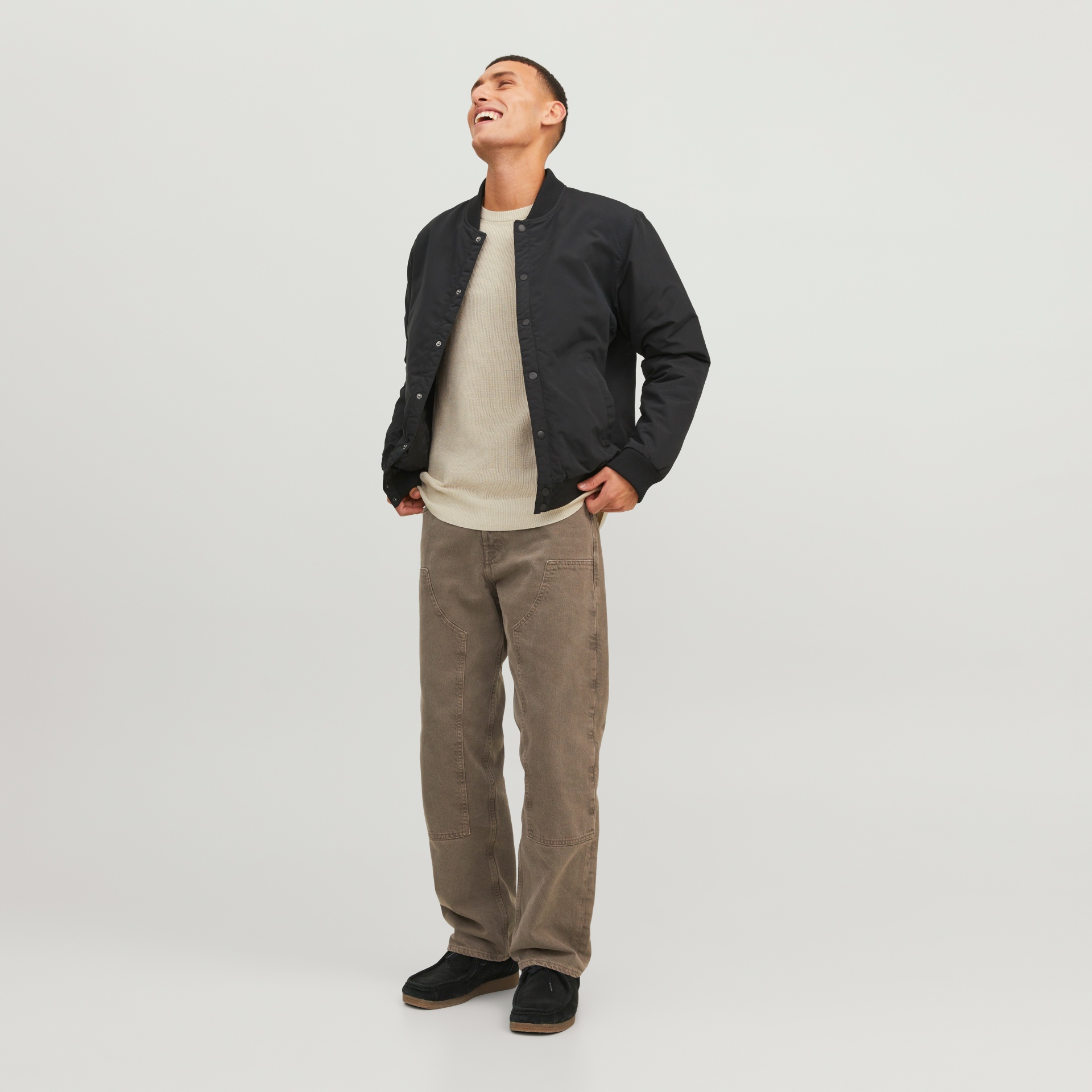 Homem com casaco preto, camisola creme, calças bege e sapatos pretos