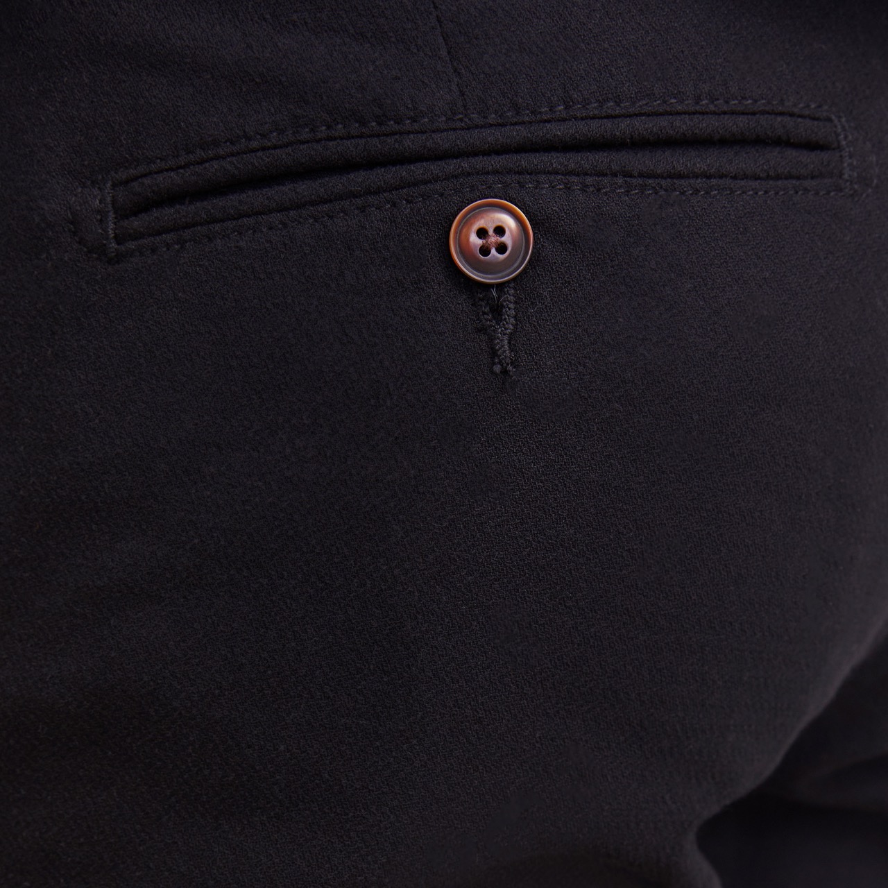 Bolso traseiro de calças pretas com botão castanho