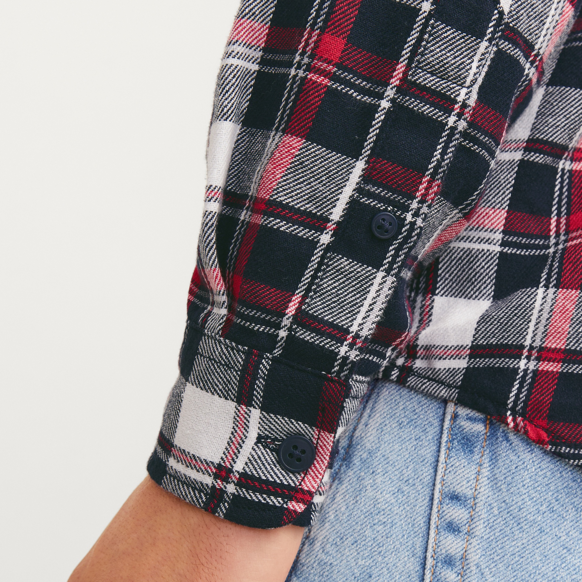 Manga de camisa xadrez vermelha, preta, branca e cinza com botões e jeans azul claro.