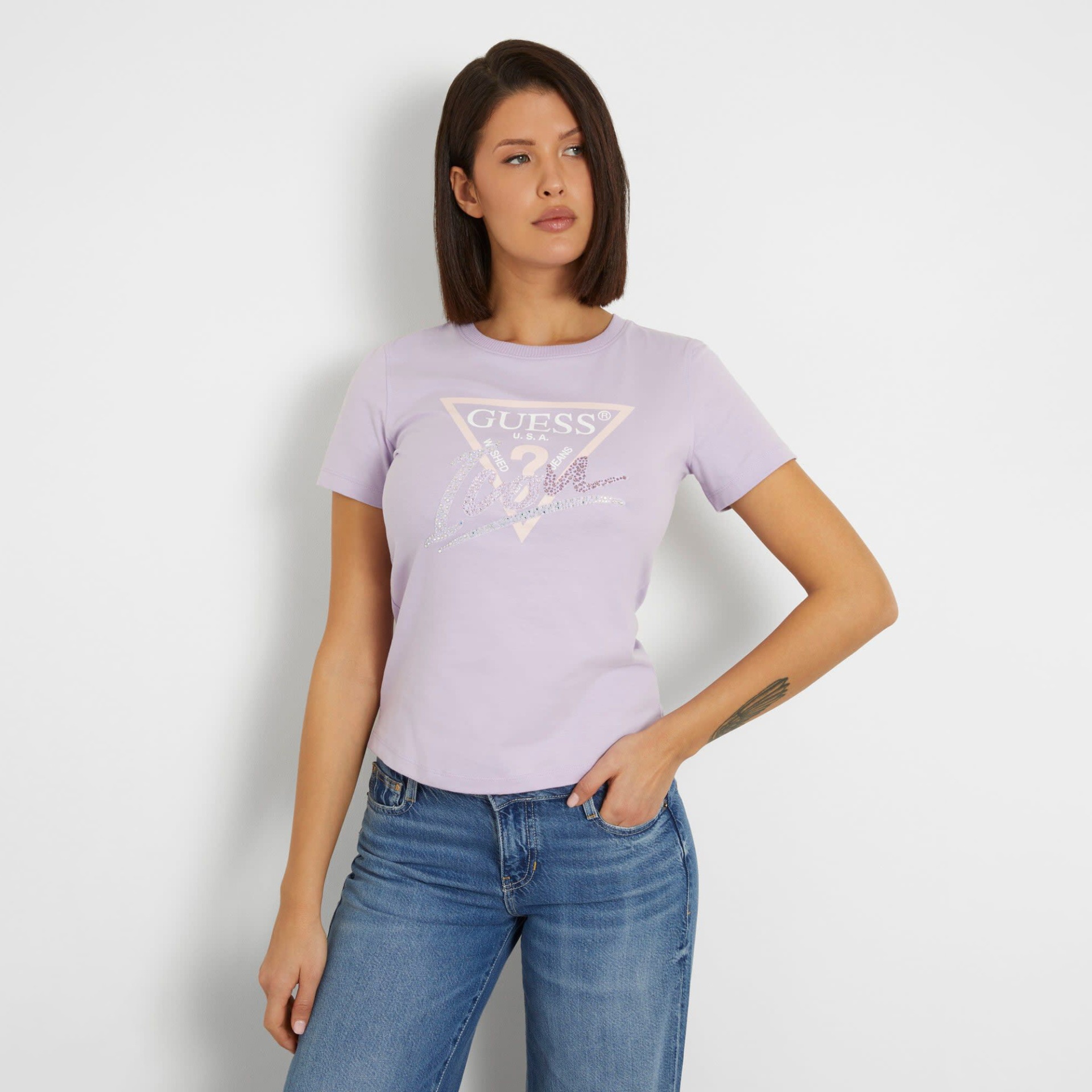 T-shirt feminina lavanda com estampado GUESS e jeans azuis