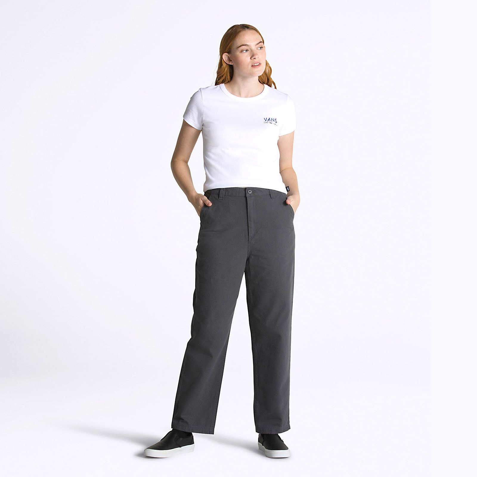 Mulher com t-shirt branca Vans, calças cinza escuras e sapatilhas pretas