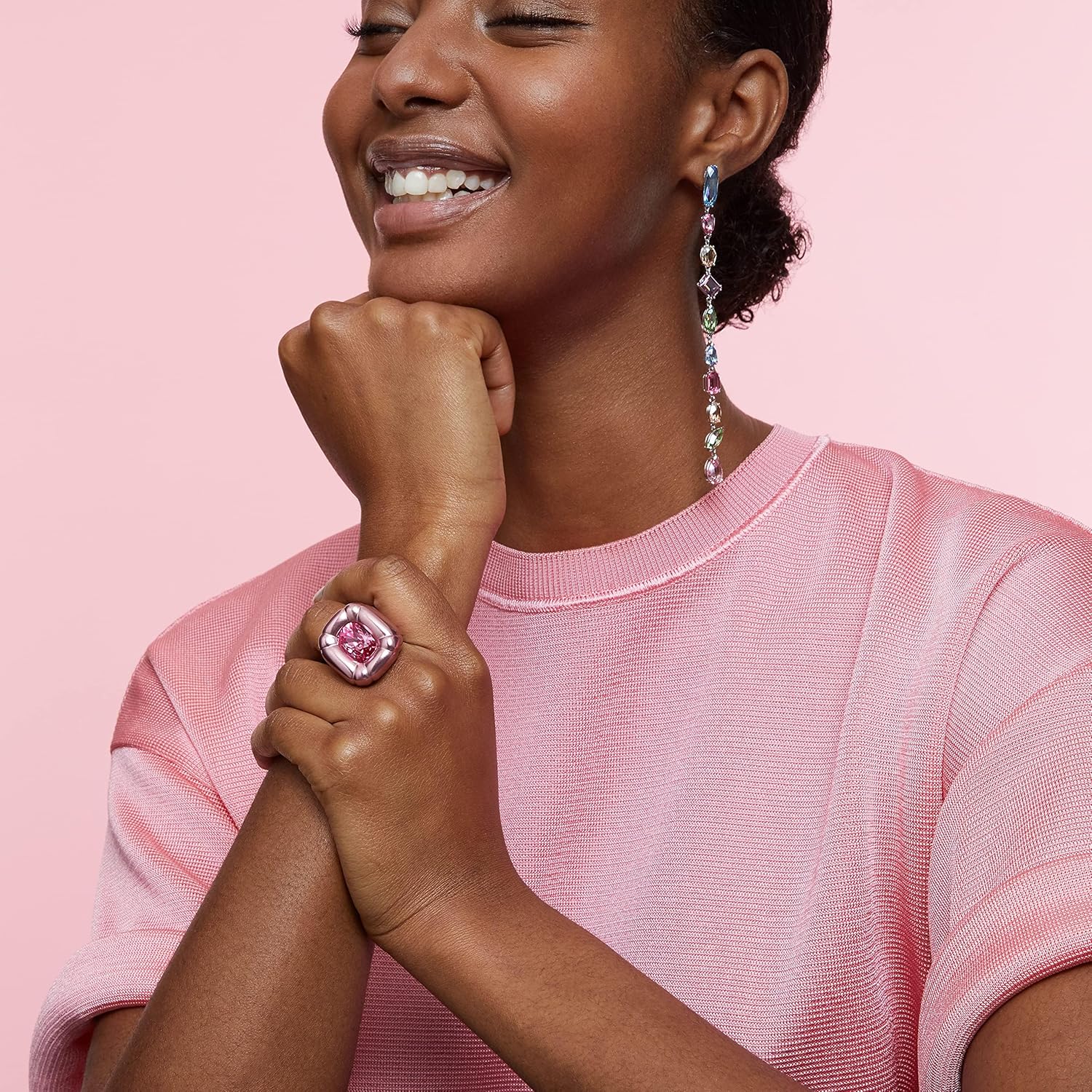 Mulher com anel rosa grande e brincos longos de pedras coloridas com camisola rosa