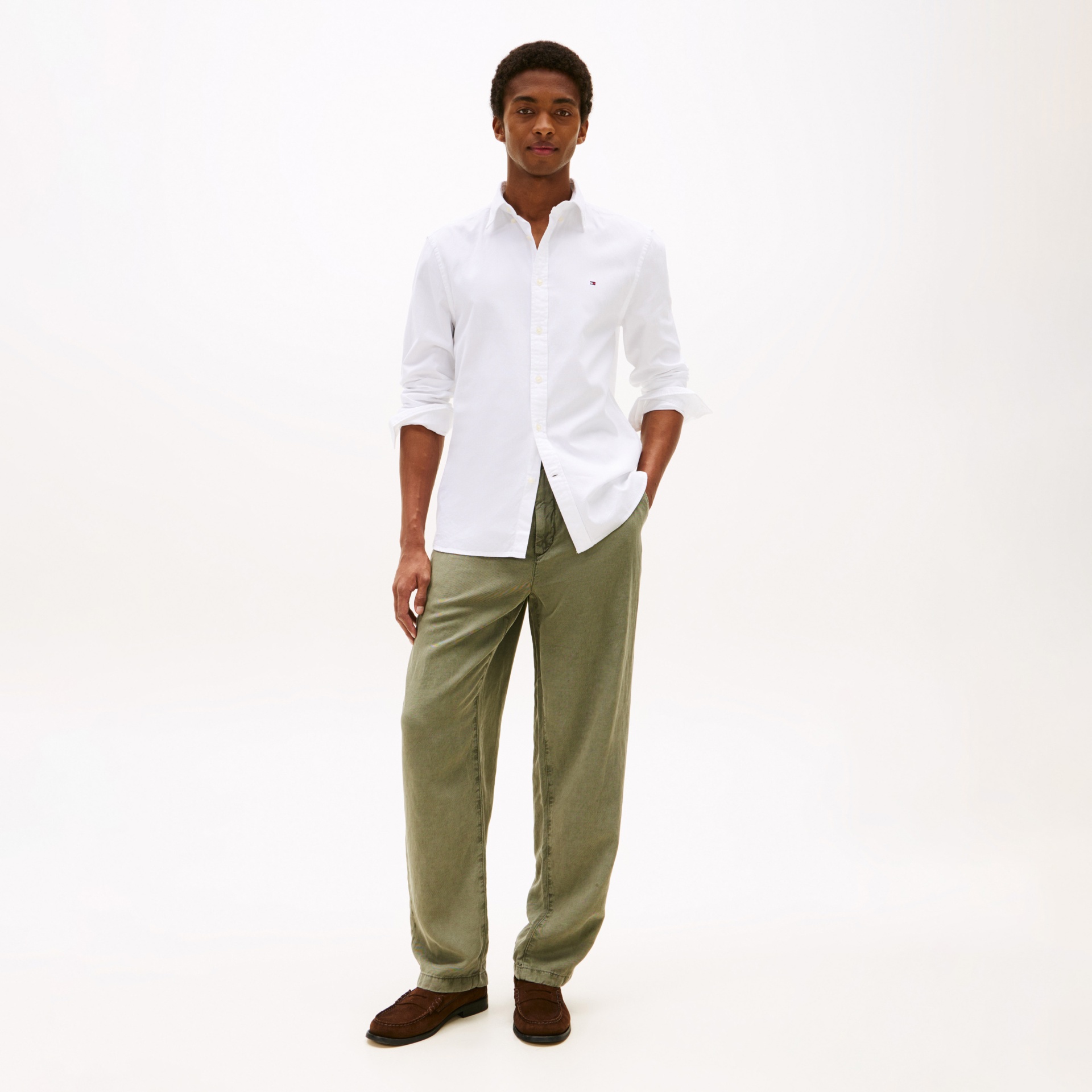 Homem com camisa branca, calças verdes largas e sapatos castanhos