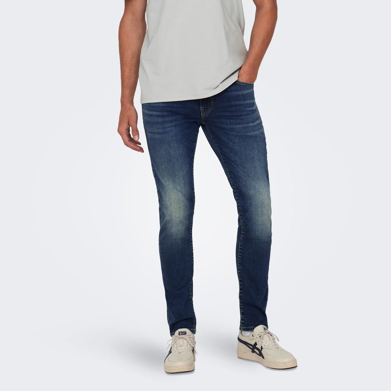 Calças de ganga azuis escuras com efeito desbotado nos joelhos e ténis brancos