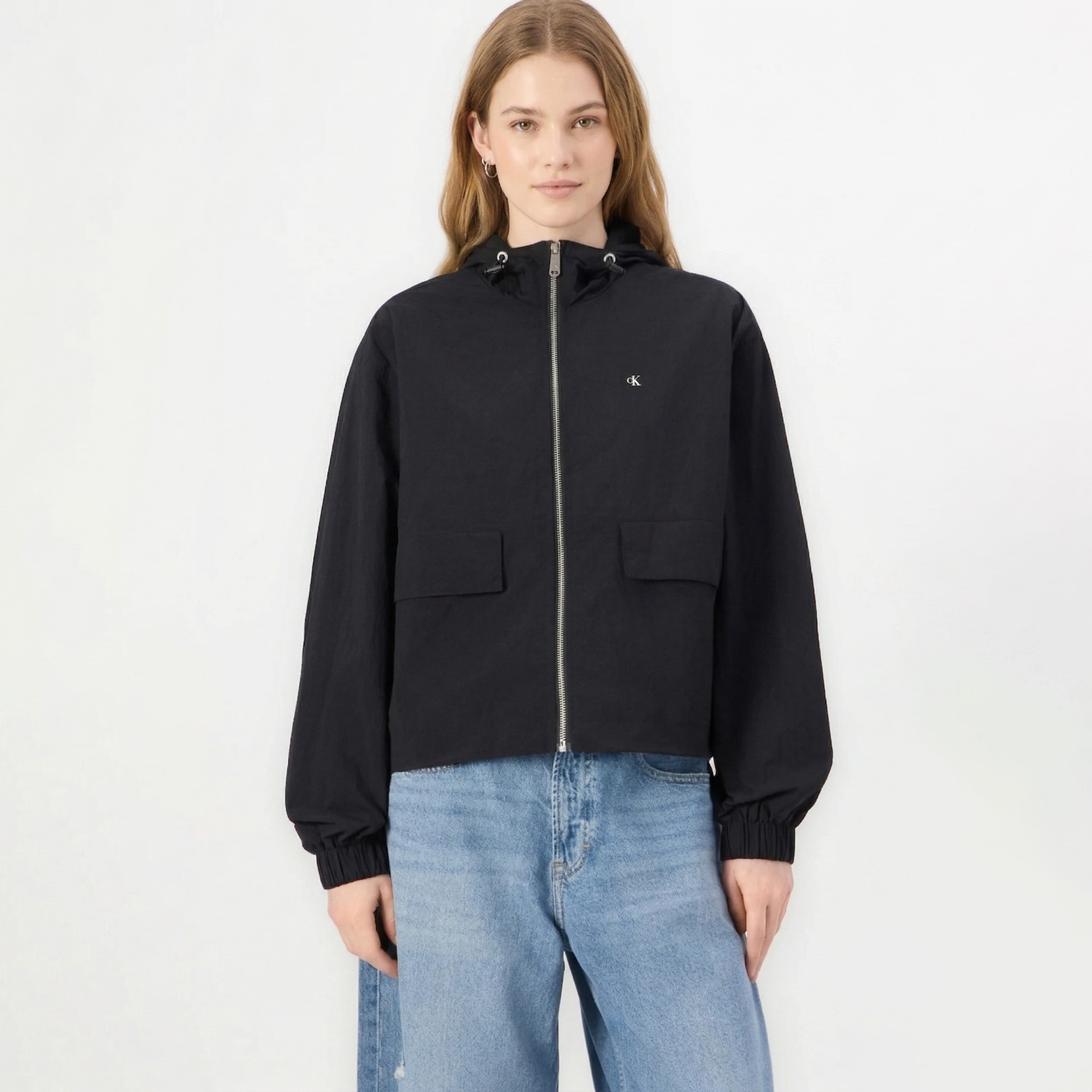 Casaco preto com fecho, capuz e logo CK, calças de ganga azul claro.