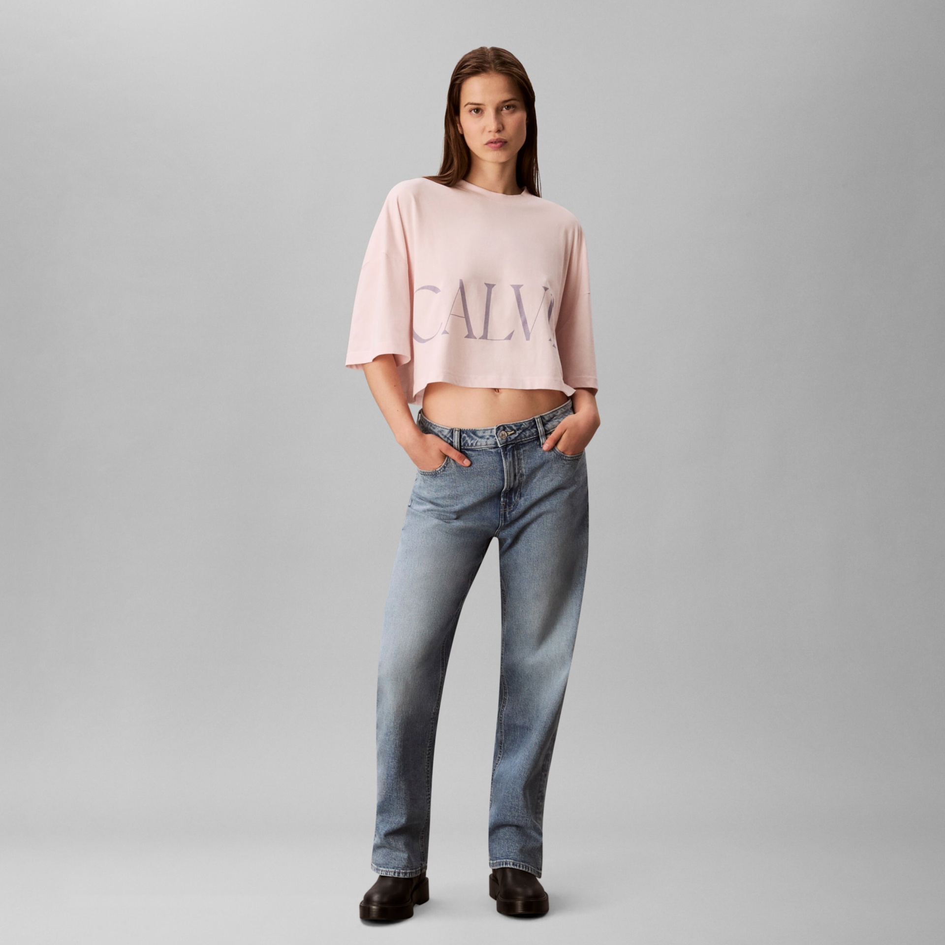 Mulher com t-shirt rosa cropped e jeans azuis claros com sapatos pretos