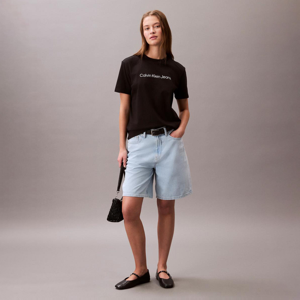 Mulher com t-shirt preta Calvin Klein Jeans, calções de ganga azul claro e mala preta