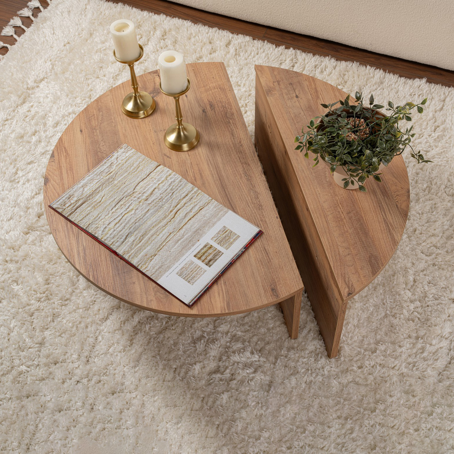 Mesa de centro redonda em madeira com castiçais, revista e planta em tapete branco.