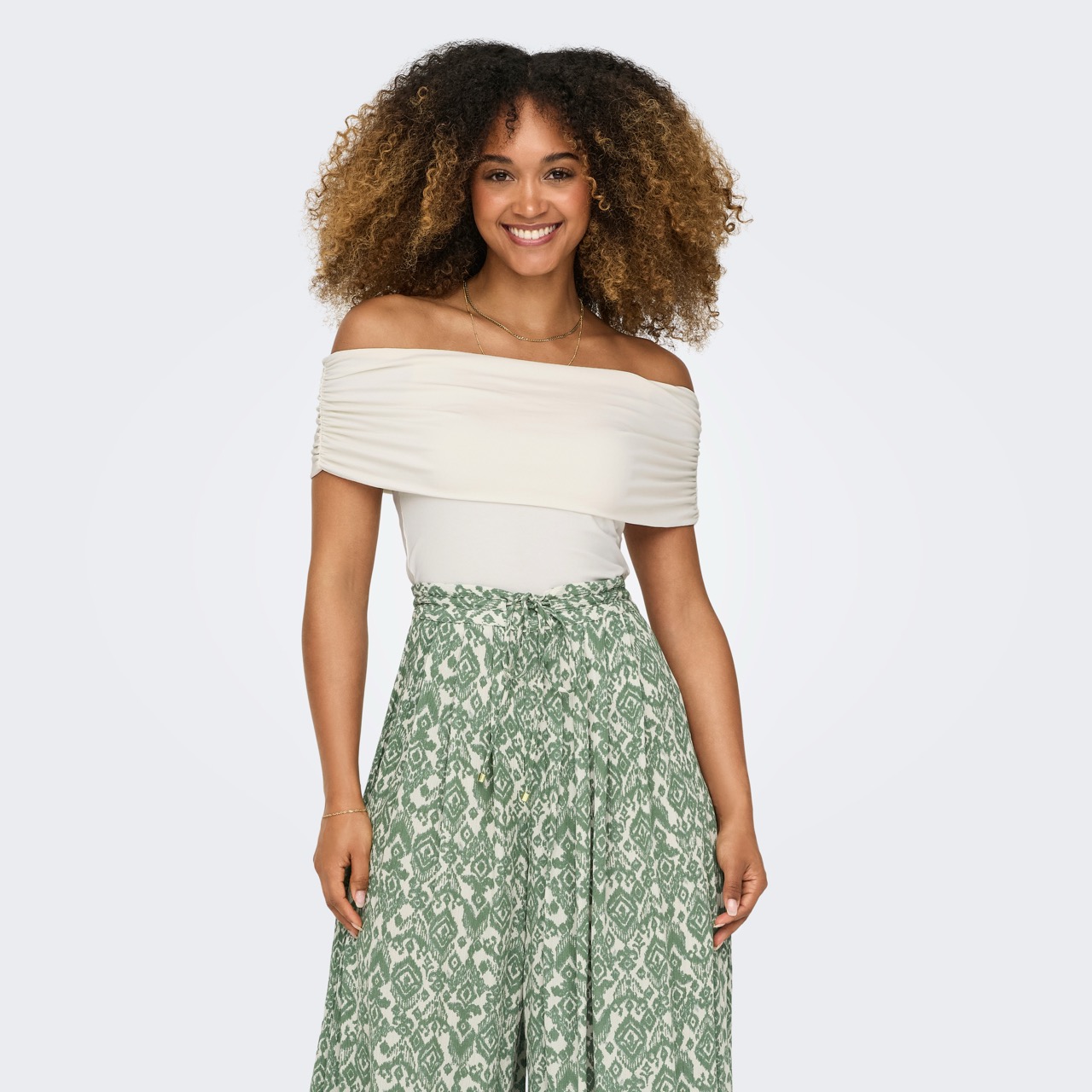 Mulher com blusa branca ombro a ombro e saia verde estampada