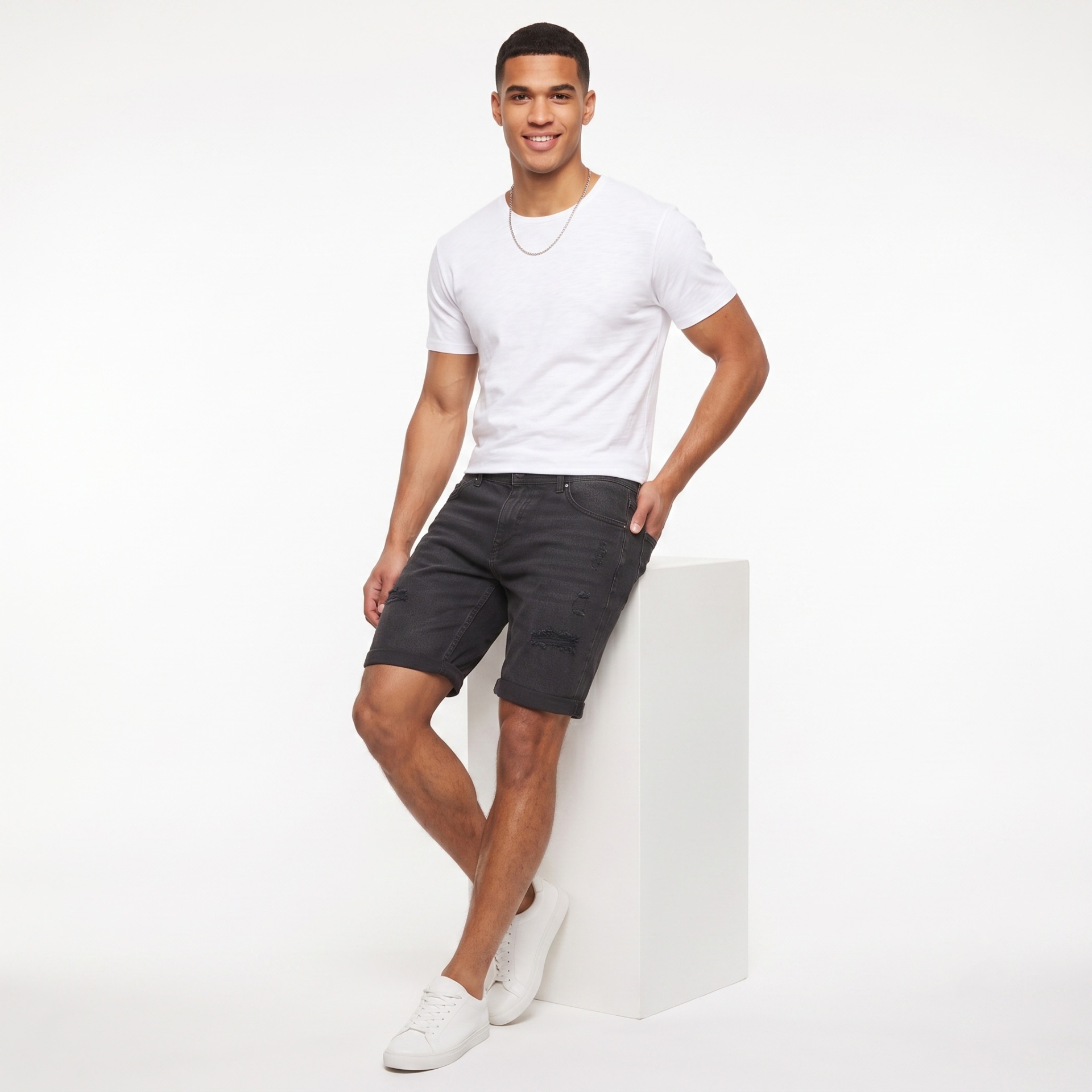 Homem com camiseta branca, bermuda preta e ténis brancos sentado