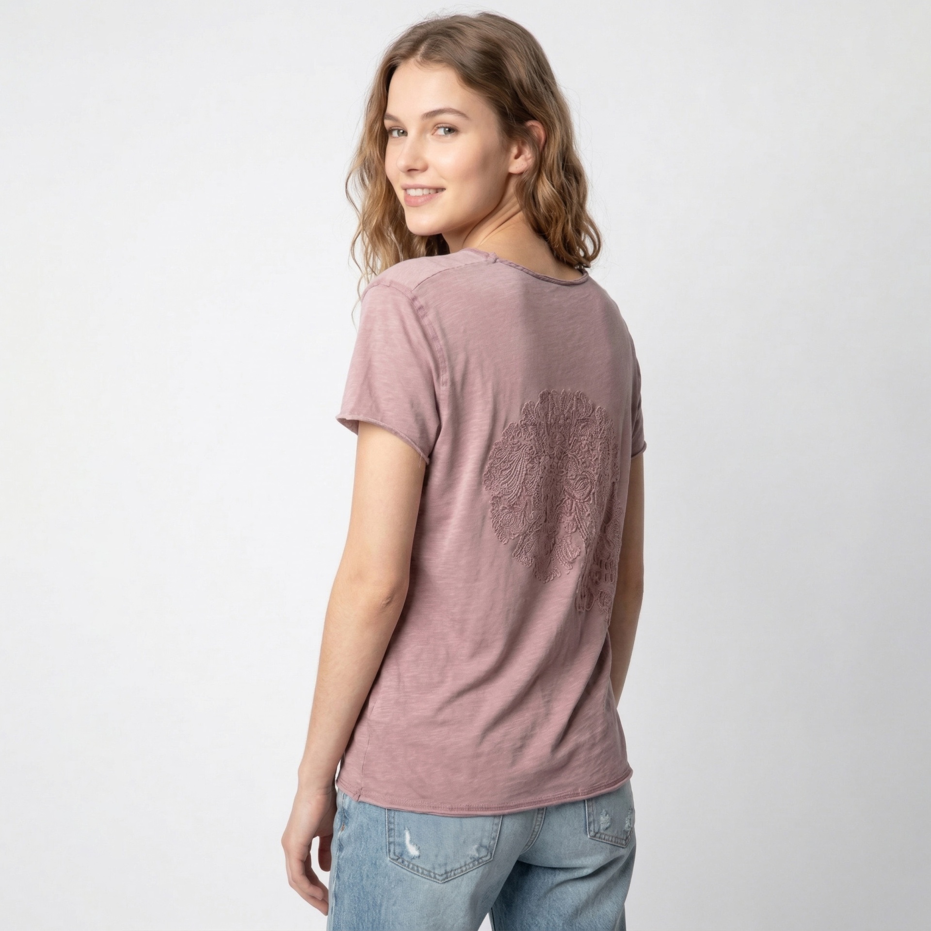 Mulher de costas a vestir t-shirt rosa antigo com bordado circular e jeans azuis claros
