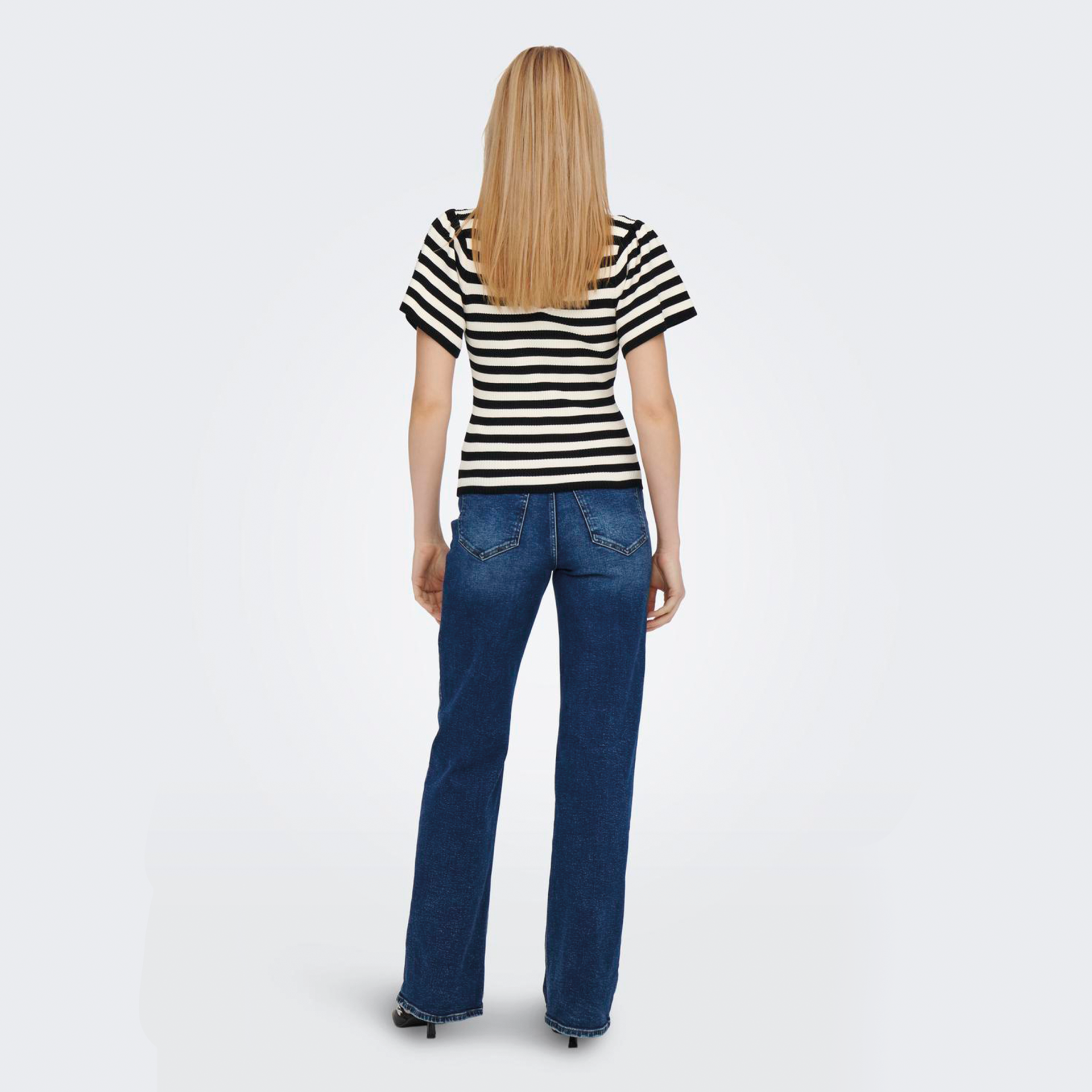 Mulher de costas com t-shirt às riscas pretas e brancas e jeans azuis.