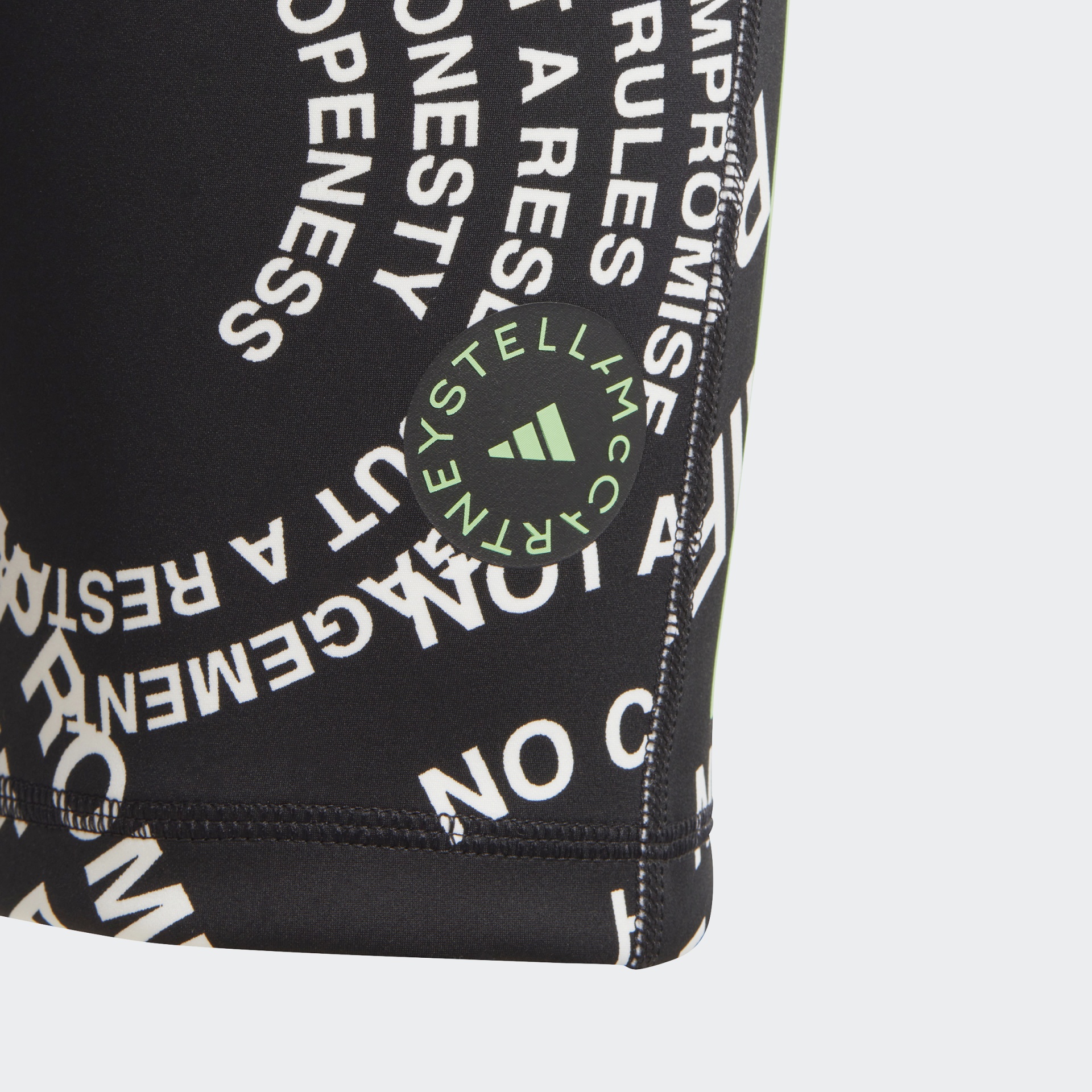 Peça de roupa preta com texto branco e selo verde com logo Adidas e Stella McCartney