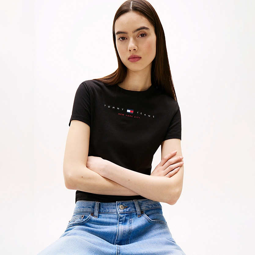 Mulher com t-shirt preta Tommy Jeans e jeans azuis claros em fundo branco