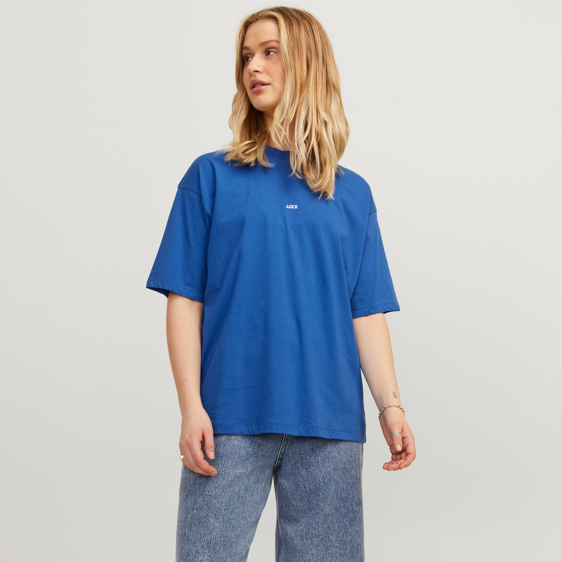 T-shirt azul com texto branco 'ACNE' e calças de ganga azuis num fundo claro