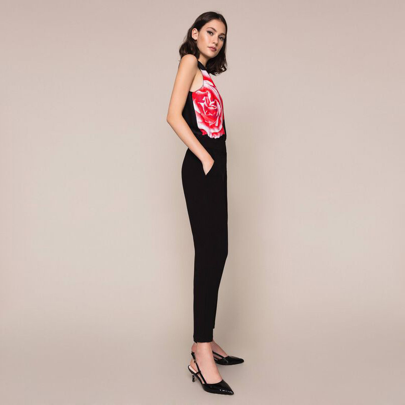 Mulher com top de alças rosa e calças pretas em fundo bege