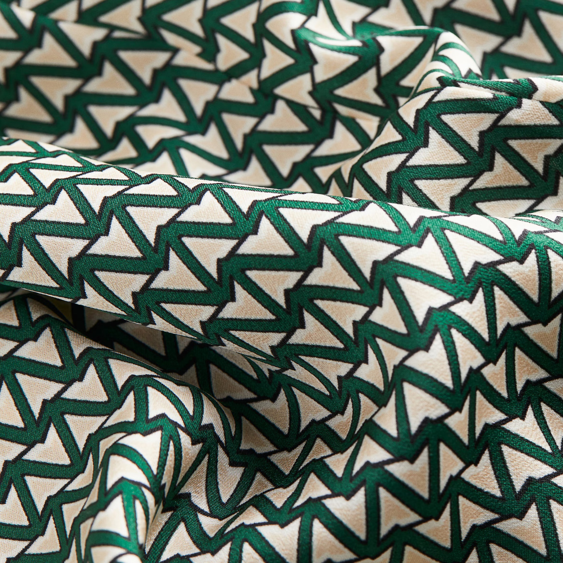 Tecido estampado com padrão geométrico em tons bege, branco e verde escuro.
