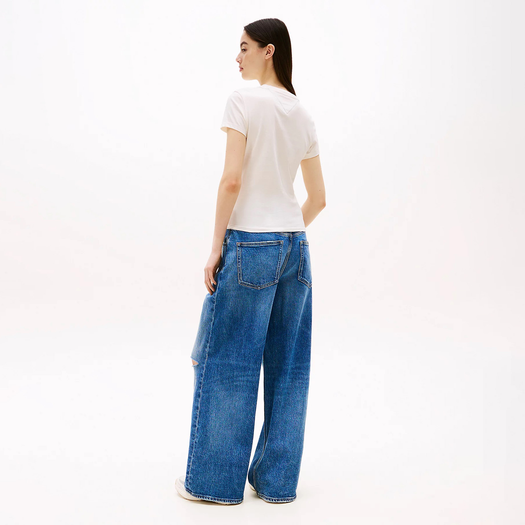 Modelo vista de costas com t-shirt branca e calças largas de ganga azuis.