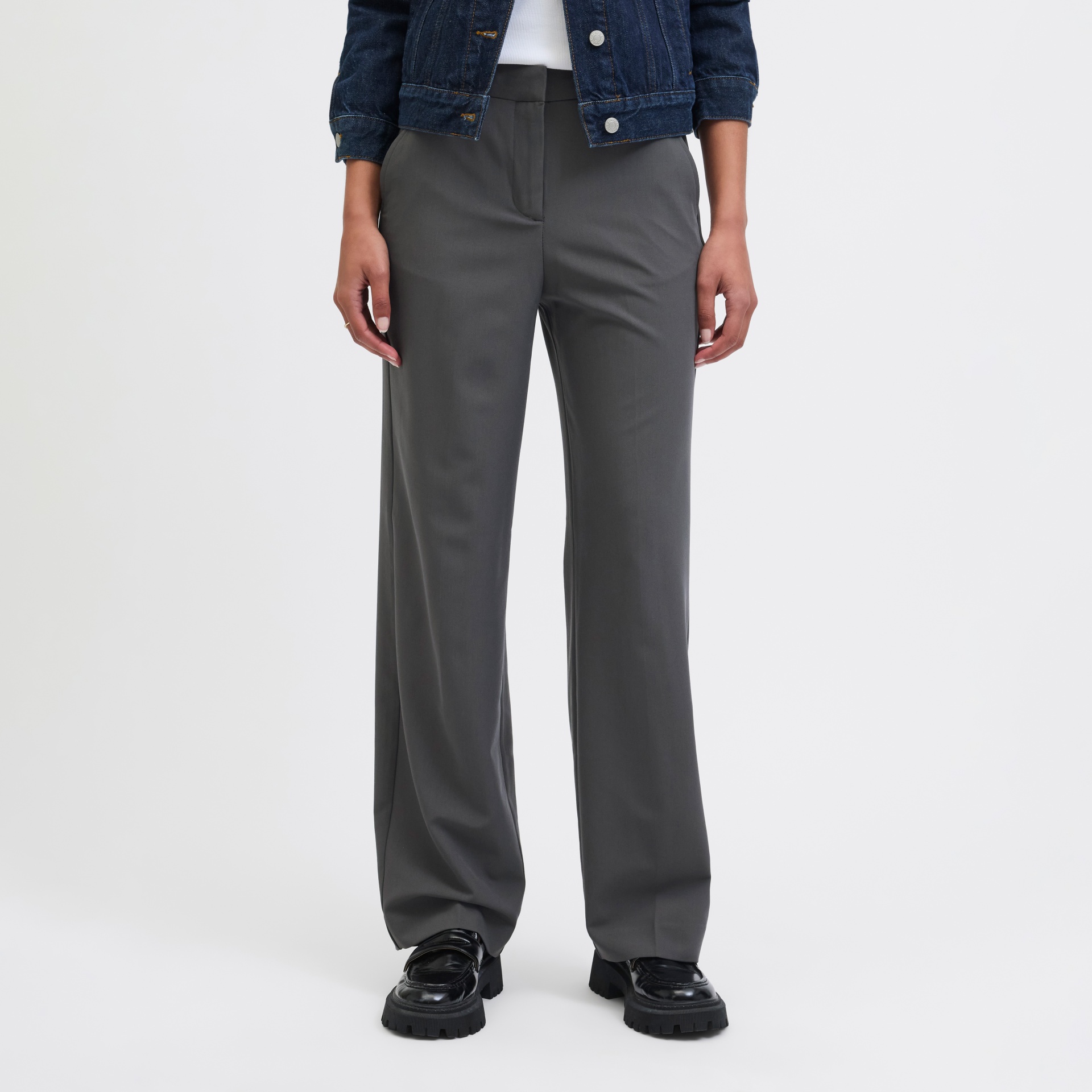 Calças cinza escuras de tecido macio com corte reto usadas com sapatos pretos e jaqueta jeans