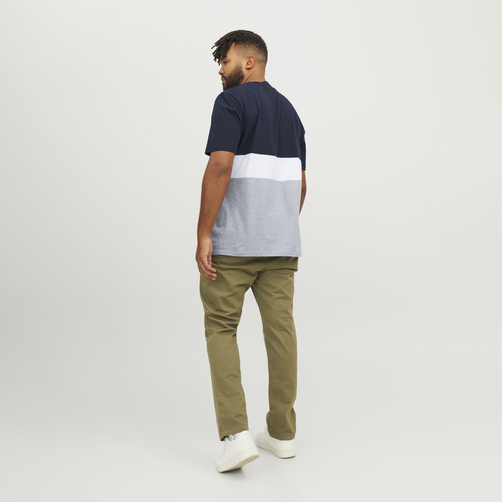 Homem de costas a usar camisola colorida, calças verdes e sapatilhas brancas.