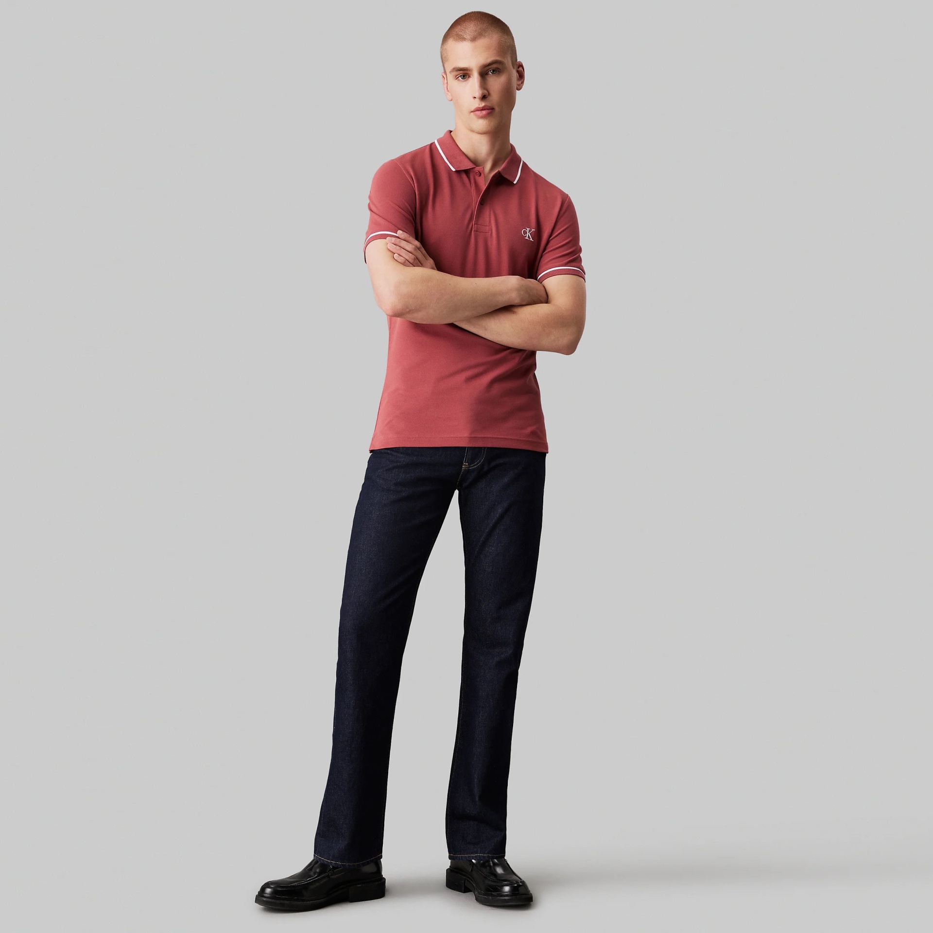 Homem com polo cor de ferrugem e calças de ganga azul escuro