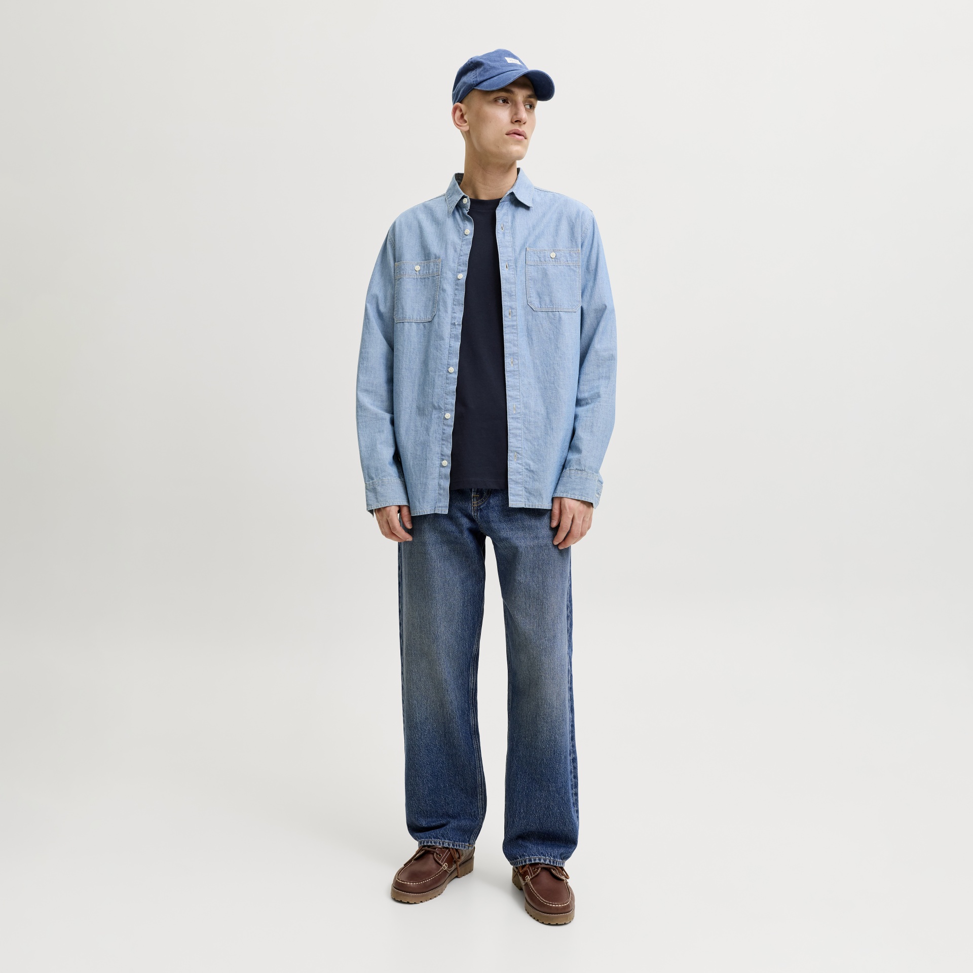 Homem com camisa azul clara, jeans largos, sapatos castanhos e boné azul