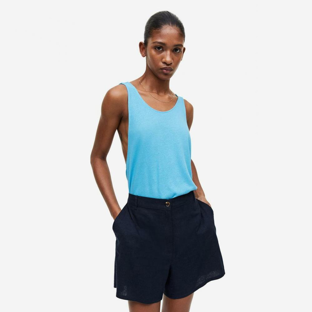 Mulher com top azul claro e calções pretos em fundo branco