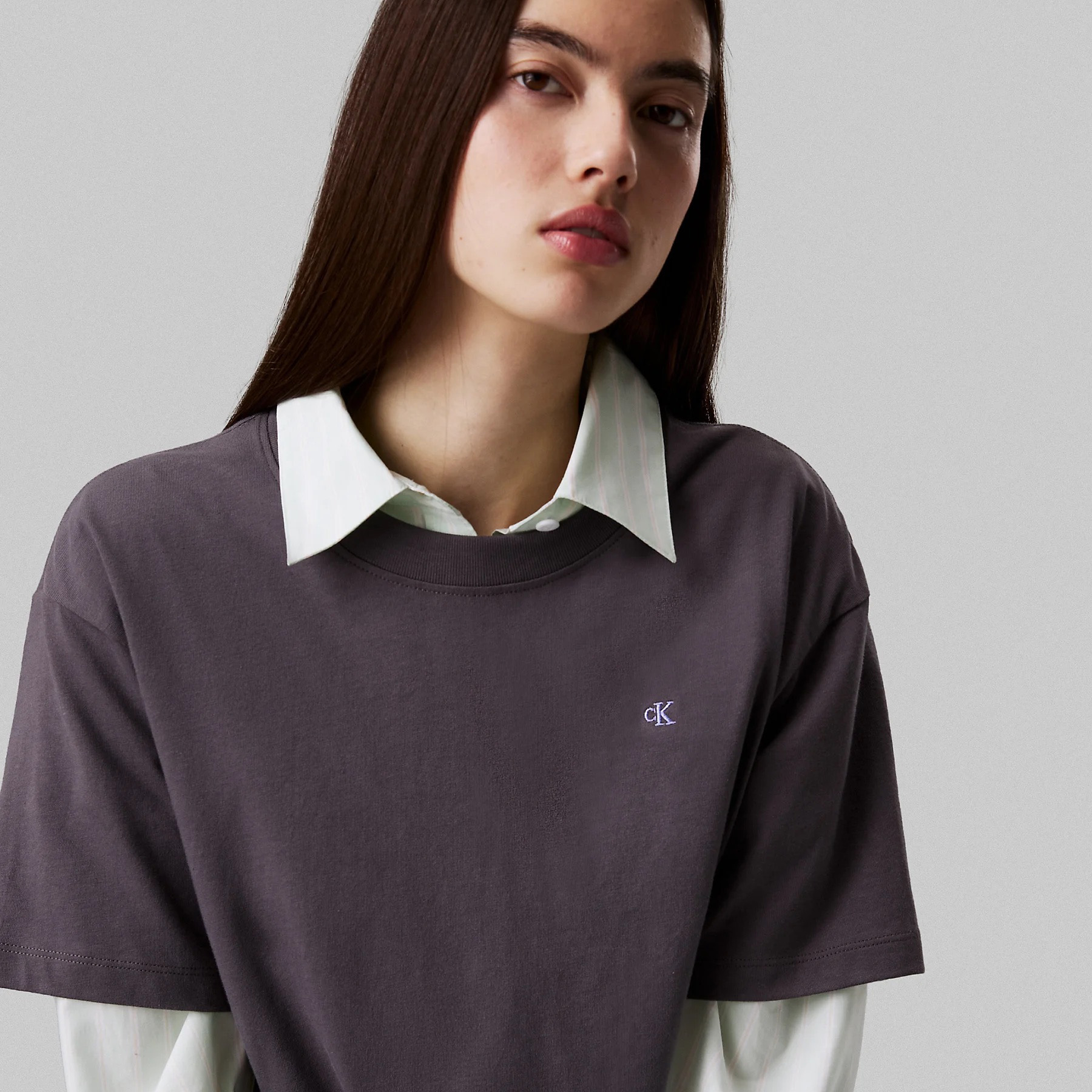 Mulher com t-shirt cinzento e camisa branca de riscas finas