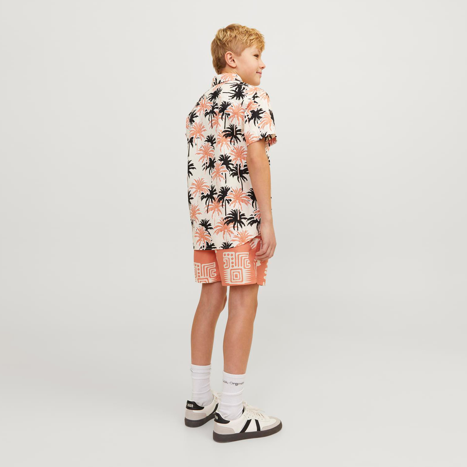 Rapaz de pé de lado com camisa e calções estampados e ténis.