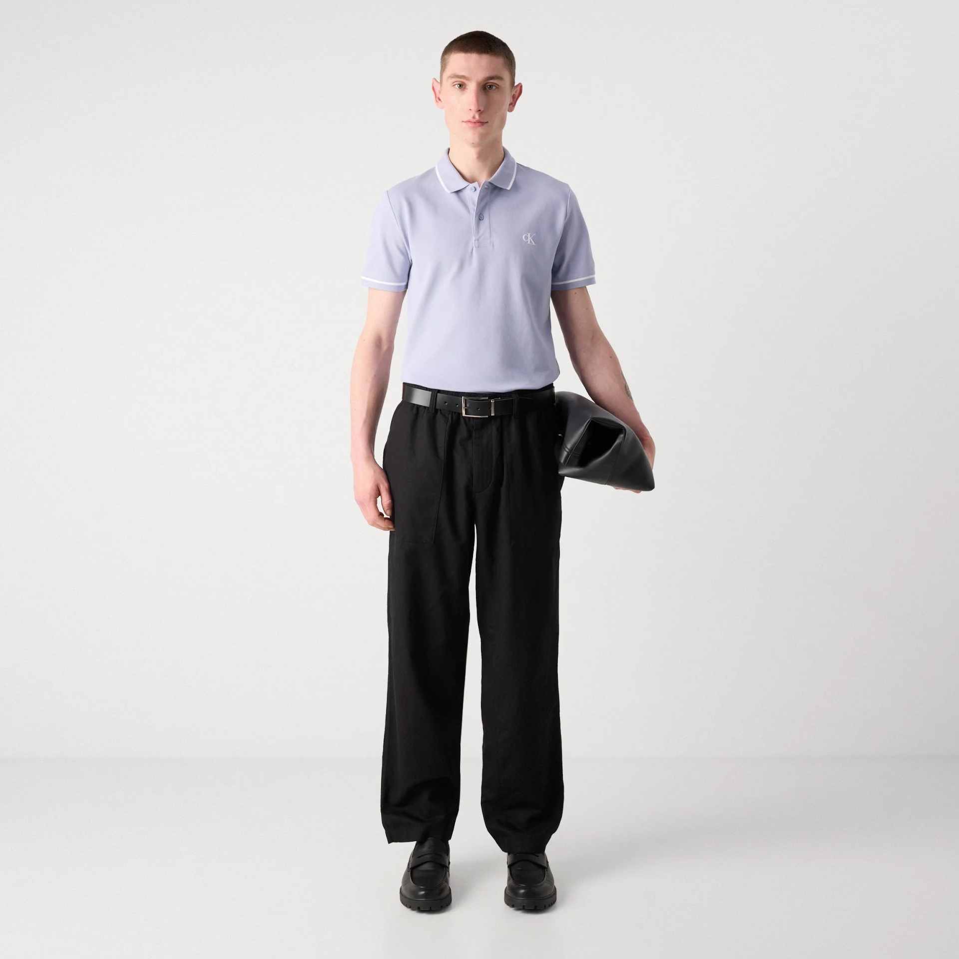 Homem com pólo lilás claro e calças largas pretas em fundo branco