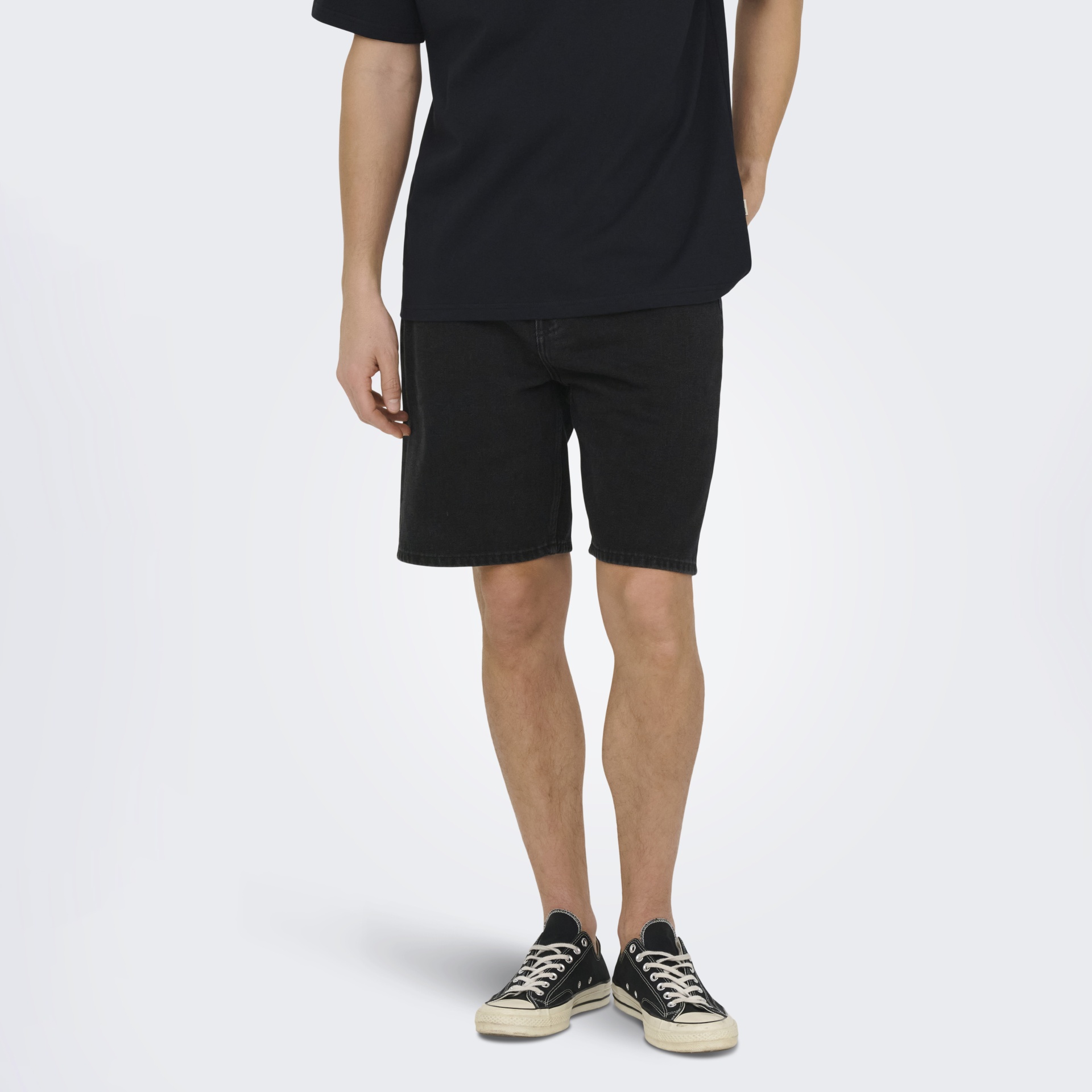 Homem com t-shirt preta, calções pretos de ganga e ténis pretos