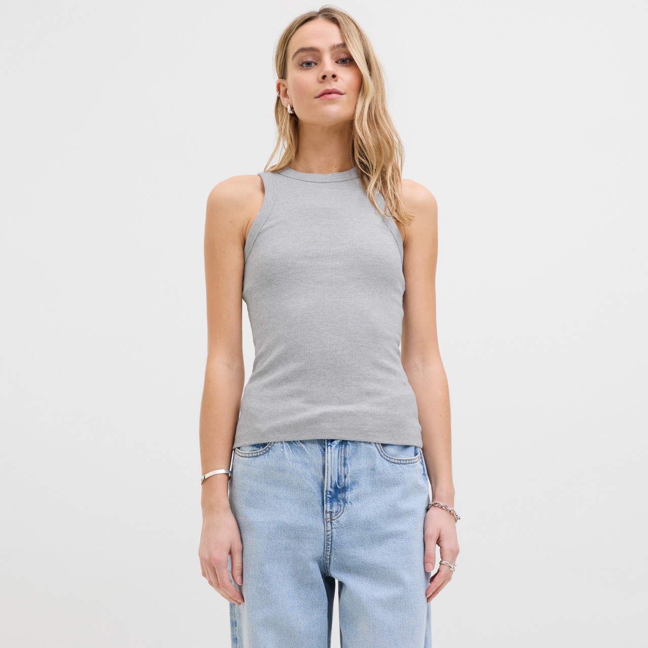 Mulher a usar top cinzento claro sem mangas com gola alta e calças de ganga azuis claras